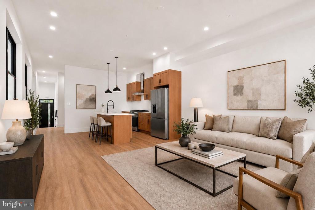 Open-plan living room and kitchen with a beige sofa, wood cabinetry, and light wood floors.