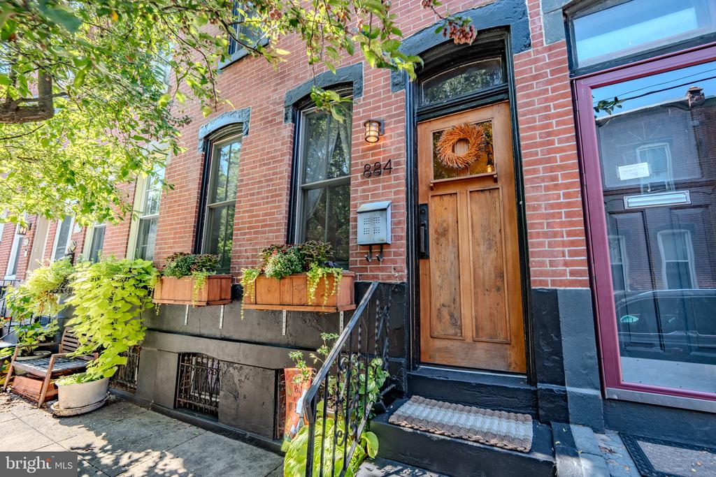Red-brick rowhouse entrance with a wreath-covered wooden door, blue trim, and planted window boxes.