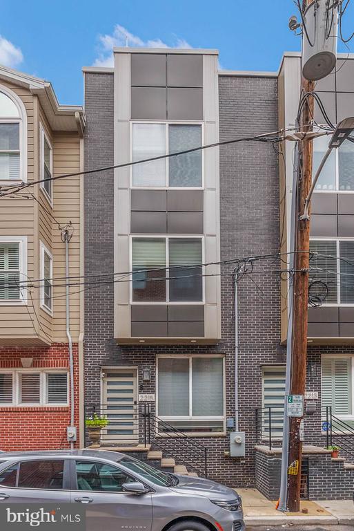 Modern brick townhouse with a tall central window bay, metal entry railings, and overhead utility wires.