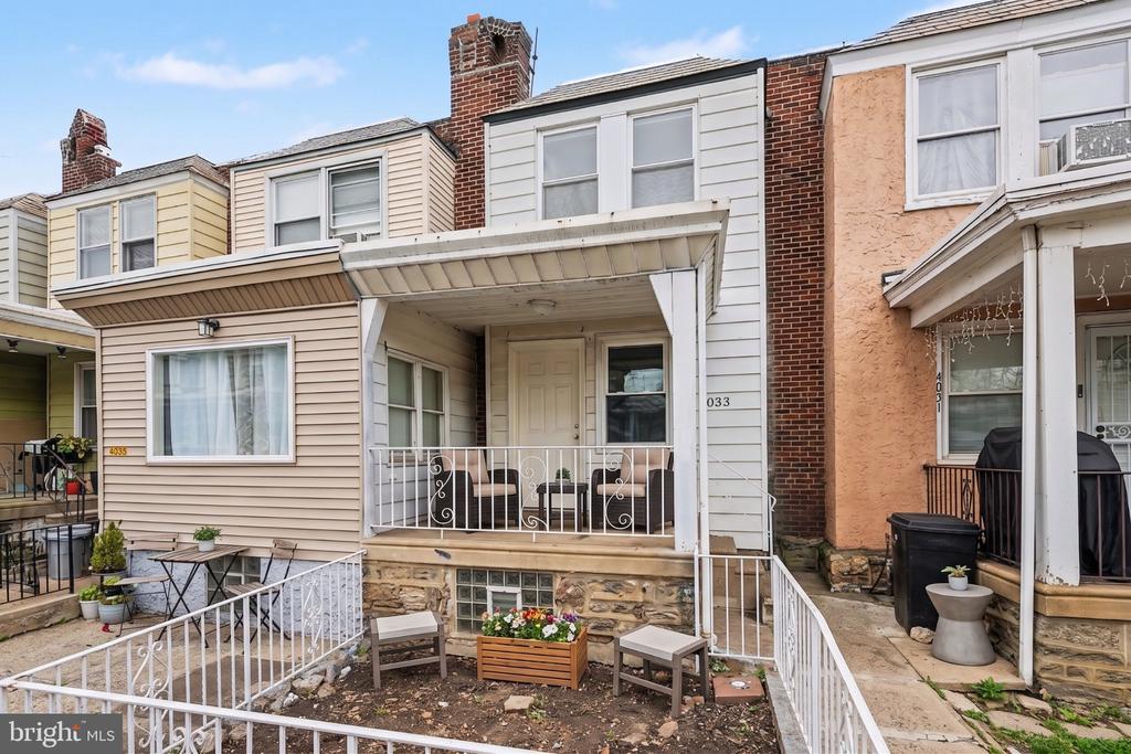 Attached row house with a covered porch, white railings, and a small front yard with patio furniture.