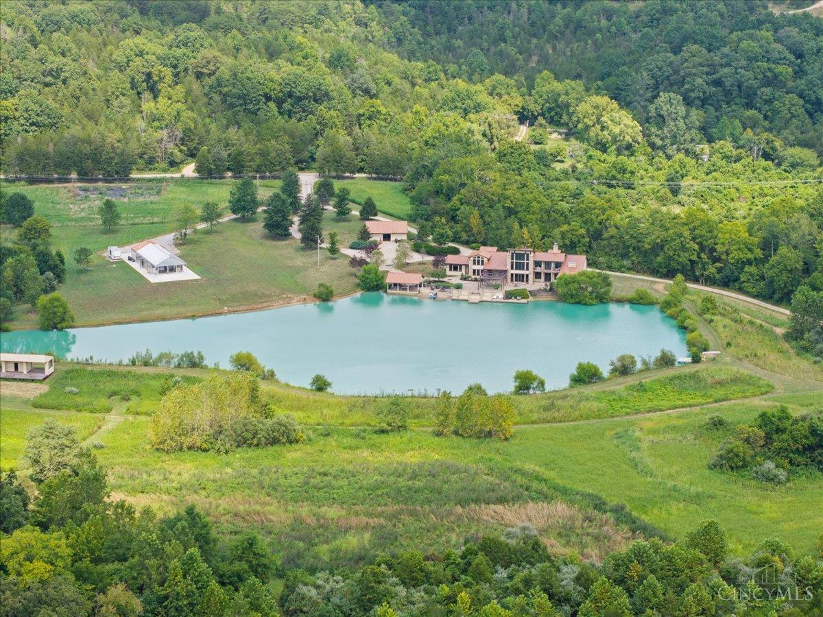 Aerial view of a wooded estate with a turquoise lake, large residence, and several outbuildings.