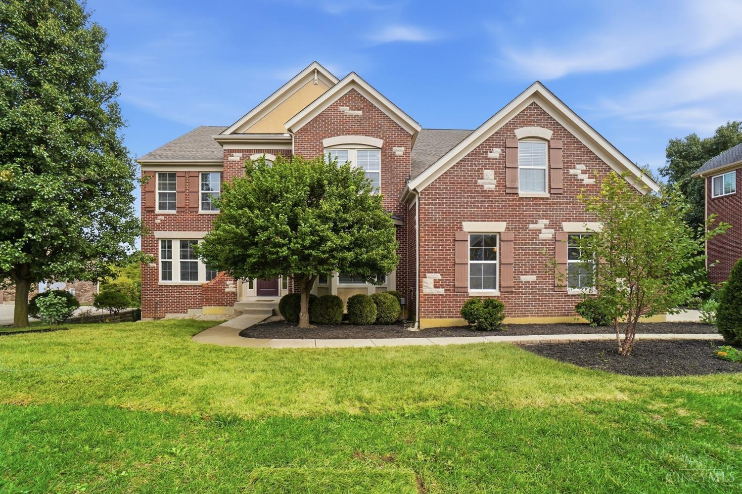 Two-story brick house with multiple gables, landscaped beds, and a broad green lawn.
