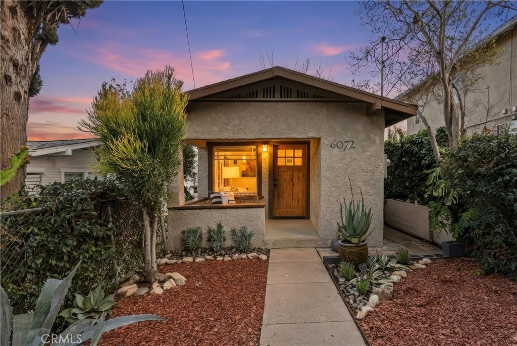 Stucco home with a lit entry and landscaped walkway at dusk.