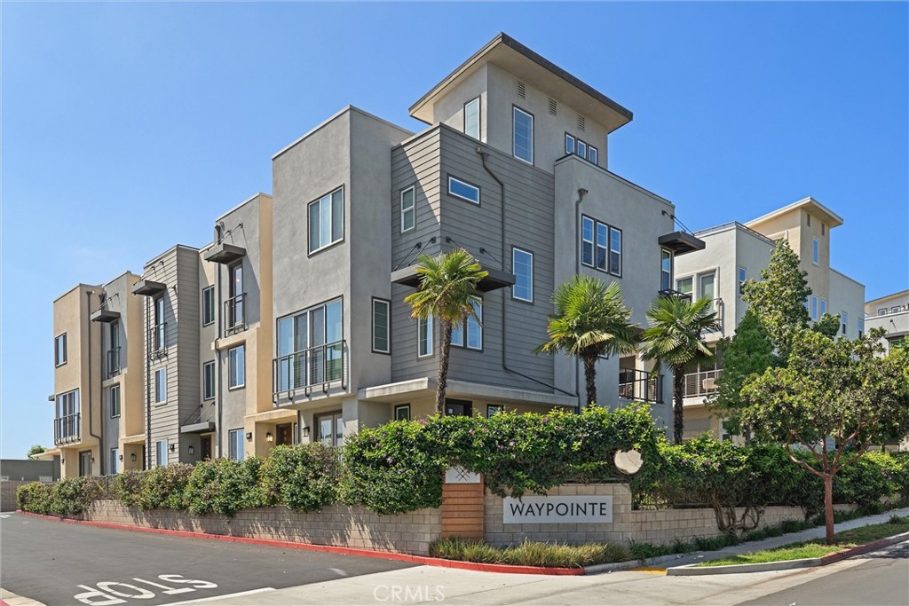 Modern gray townhomes at Waypointe, with balconies, palm trees, and a landscaped wall.