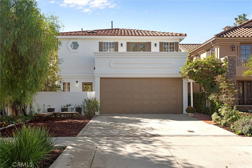 Two-story white stucco home with a tiled roof, wide garage, and landscaped driveway.