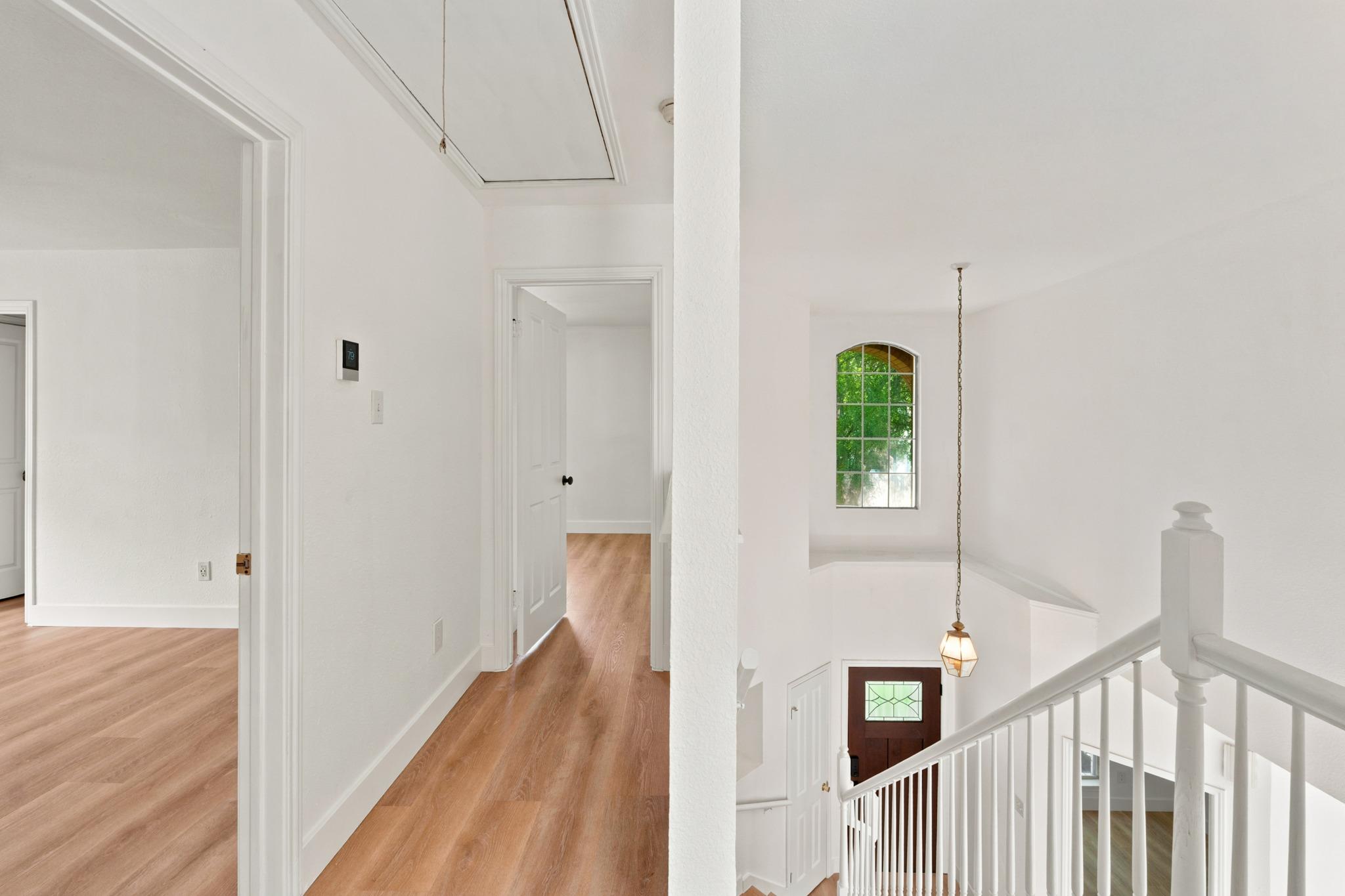 Upstairs hallway overlooking a foyer and staircase, with warm wood floors and an arched window.
