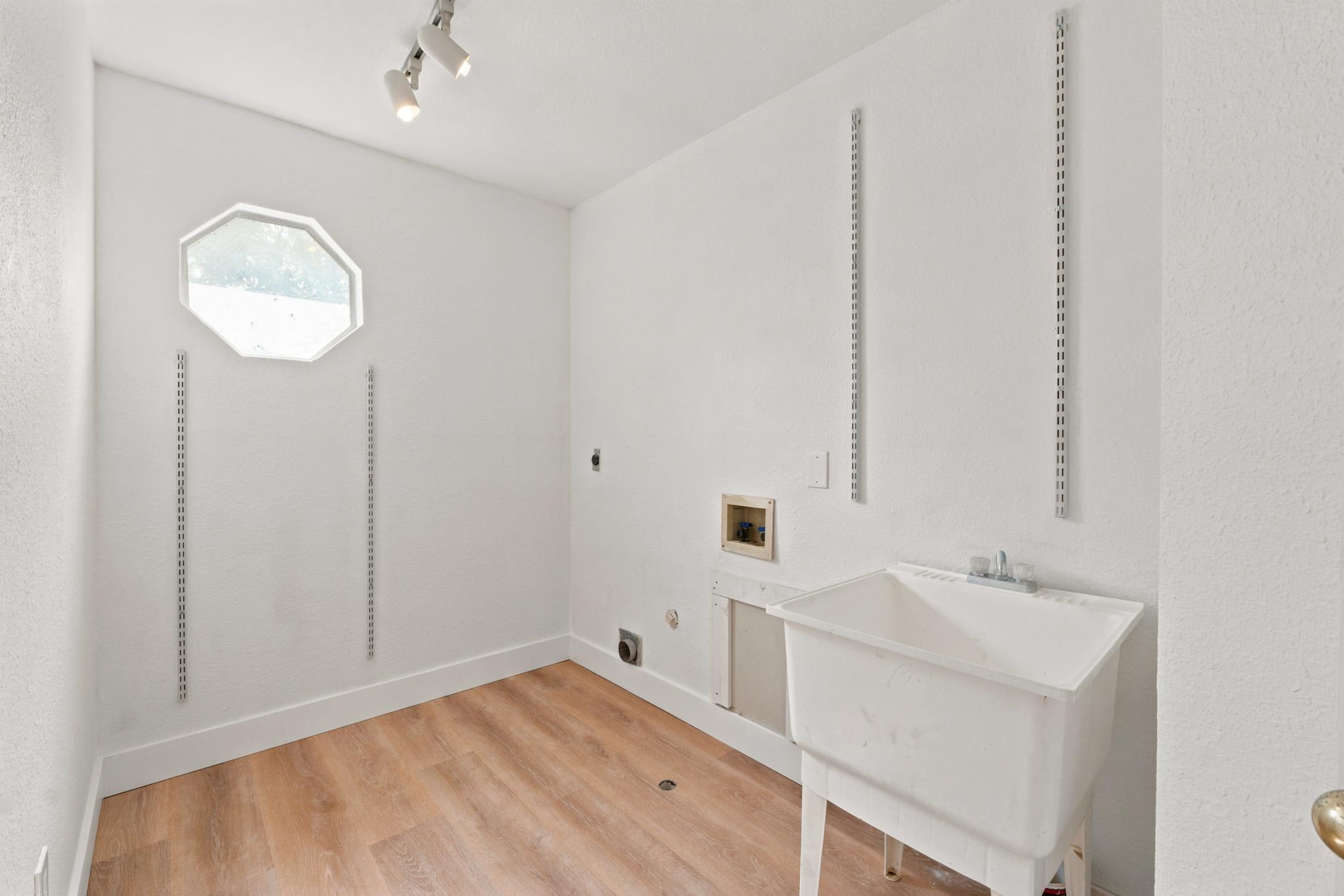 Laundry room with a large utility sink, wood-look flooring, and an octagonal window.