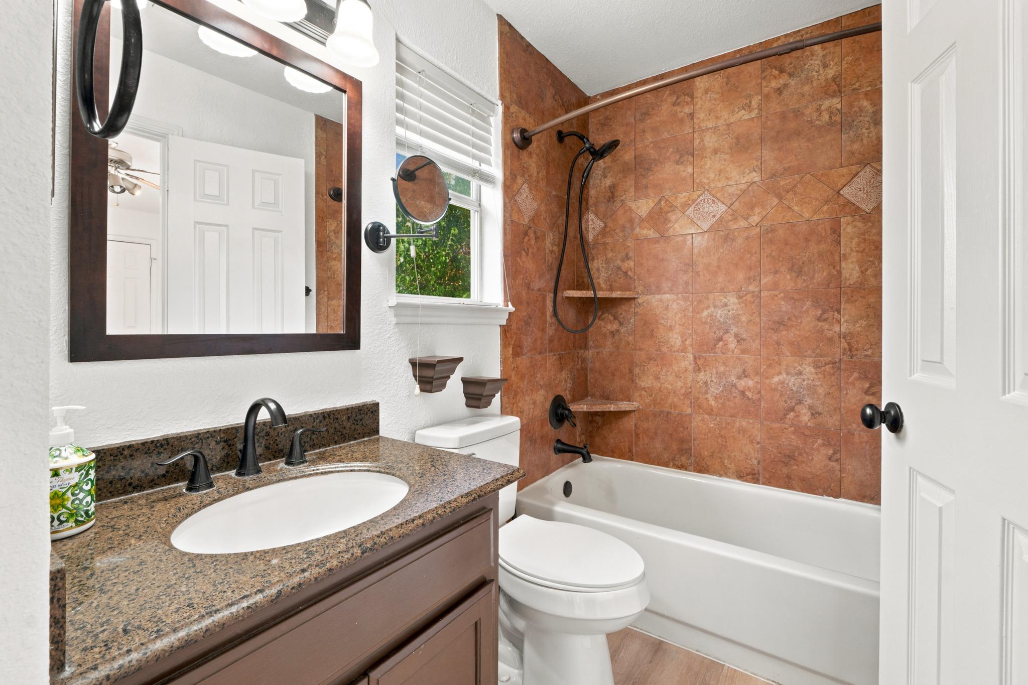 Bathroom with a granite vanity and brown tiled tub-and-shower surround.