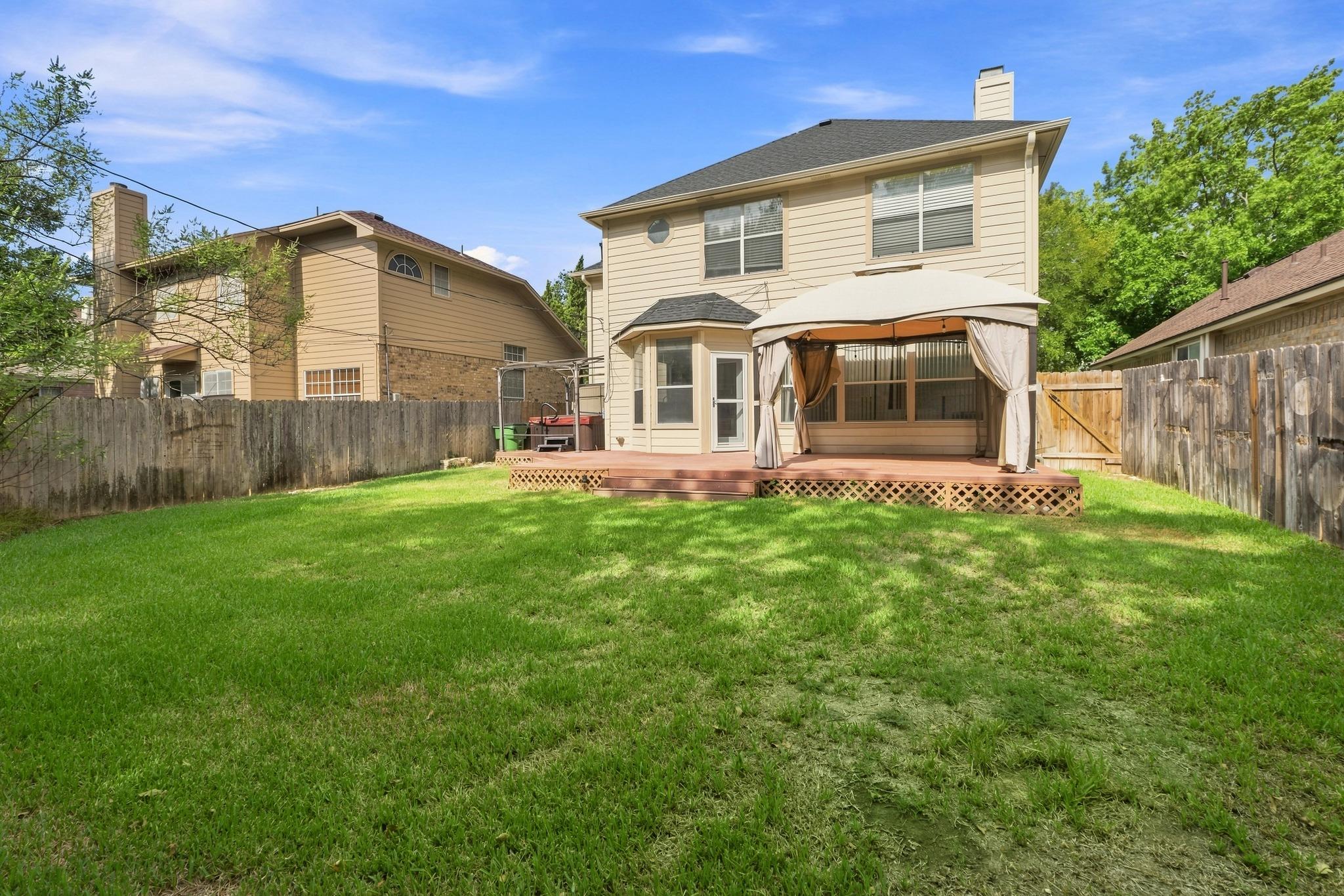 Backyard lawn and fenced deck with a curtained canopy behind a two-story beige house.