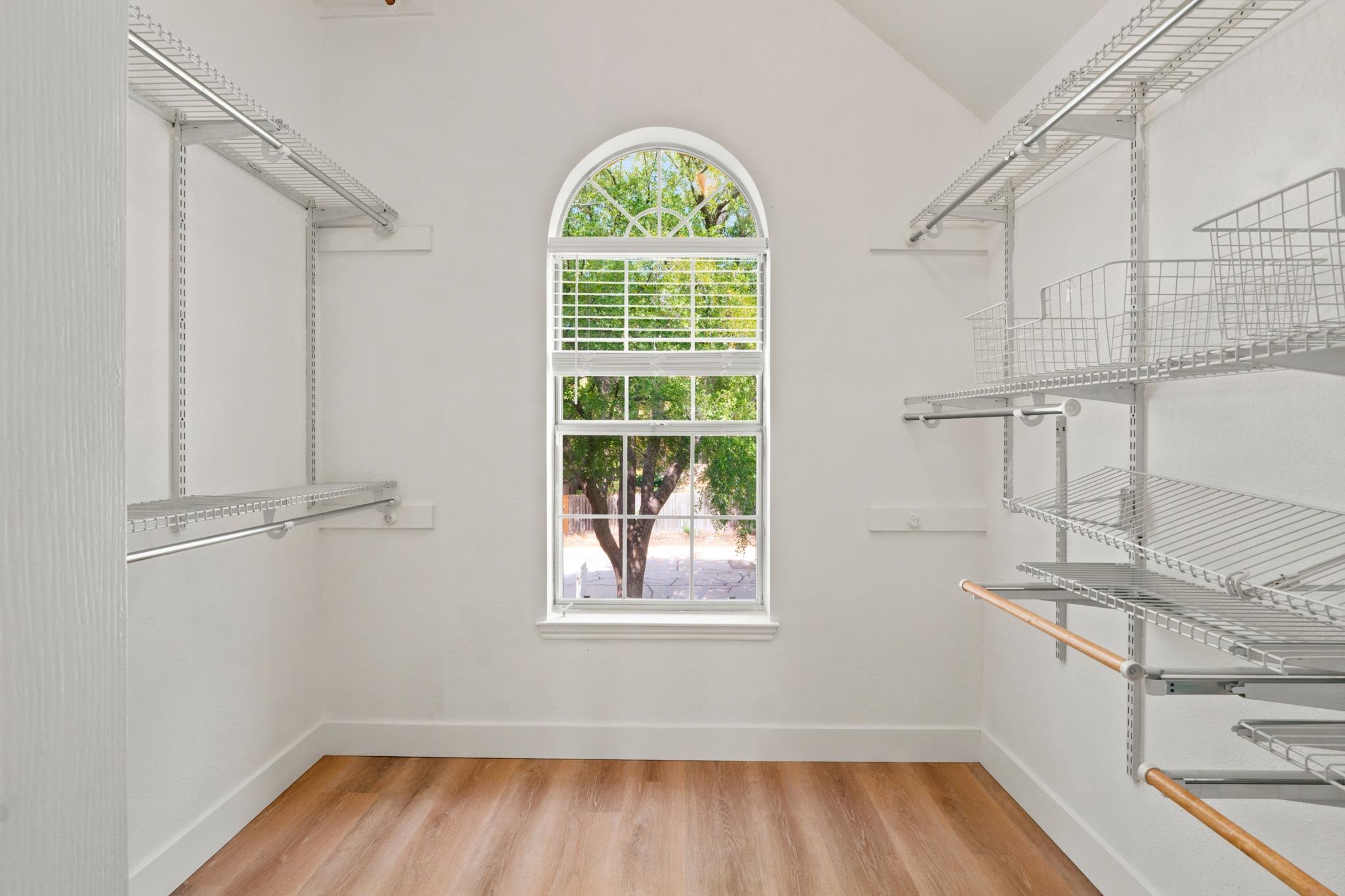 Walk-in closet with wire shelving on both sides and a tall arched window overlooking trees.