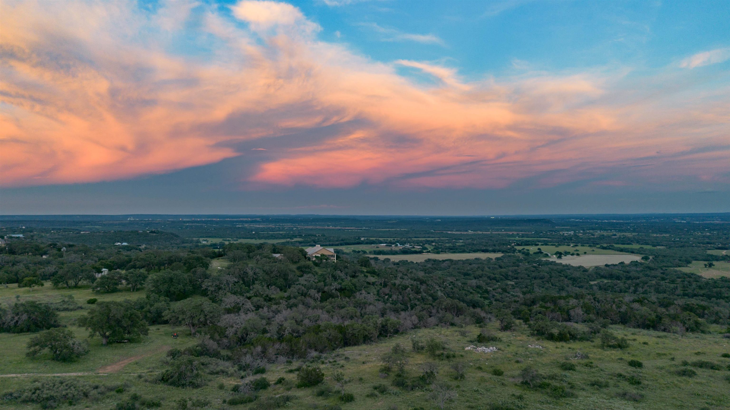 Aerial view of wooded rural acreage and open fields beneath a pink sunset sky.