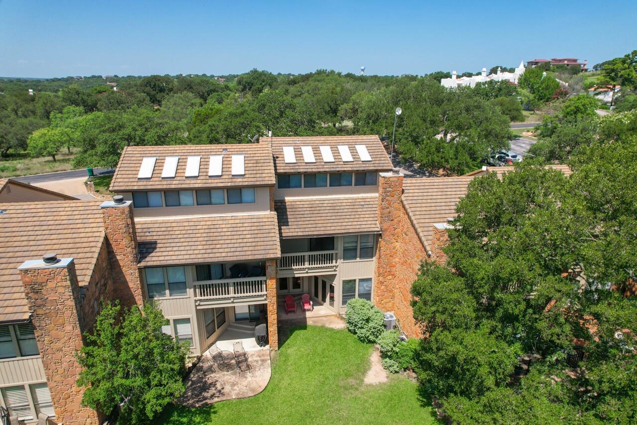Aerial view of a multi-story home with stone chimneys, roof skylights, balconies and a lawn.