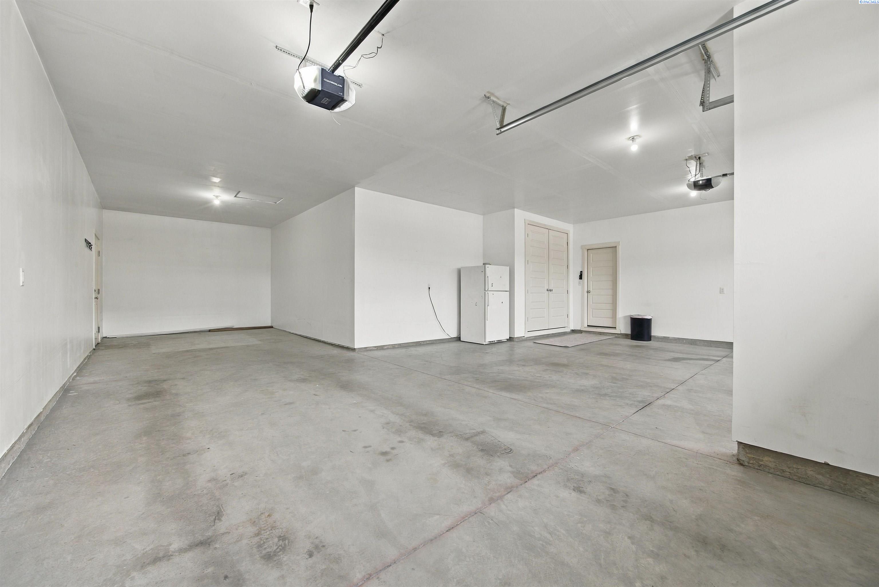 Vacant garage with a concrete floor, two garage door openers, and a refrigerator.