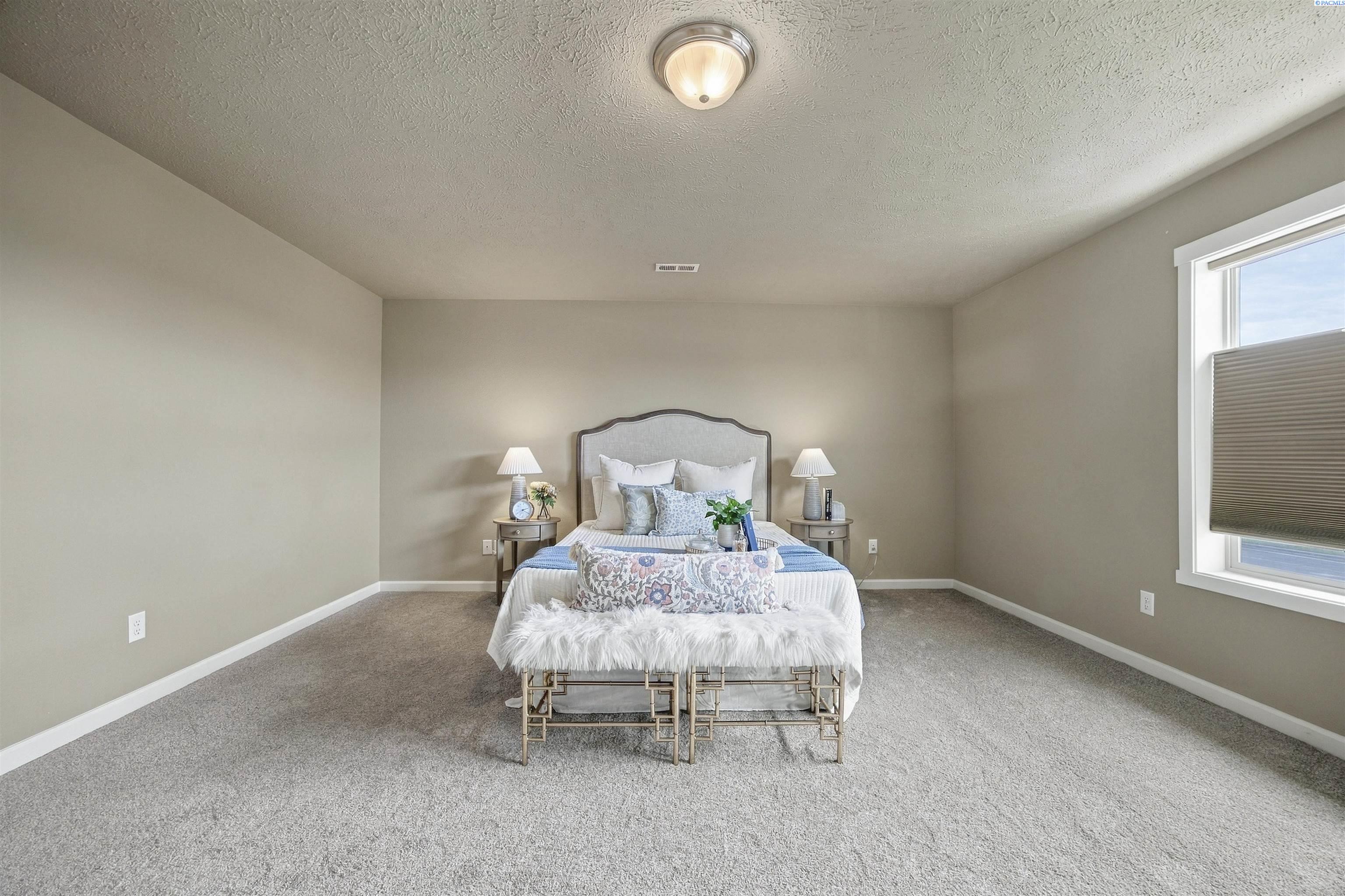 Staged bedroom with a centered bed, matching bedside lamps, and a large window with a lowered shade.