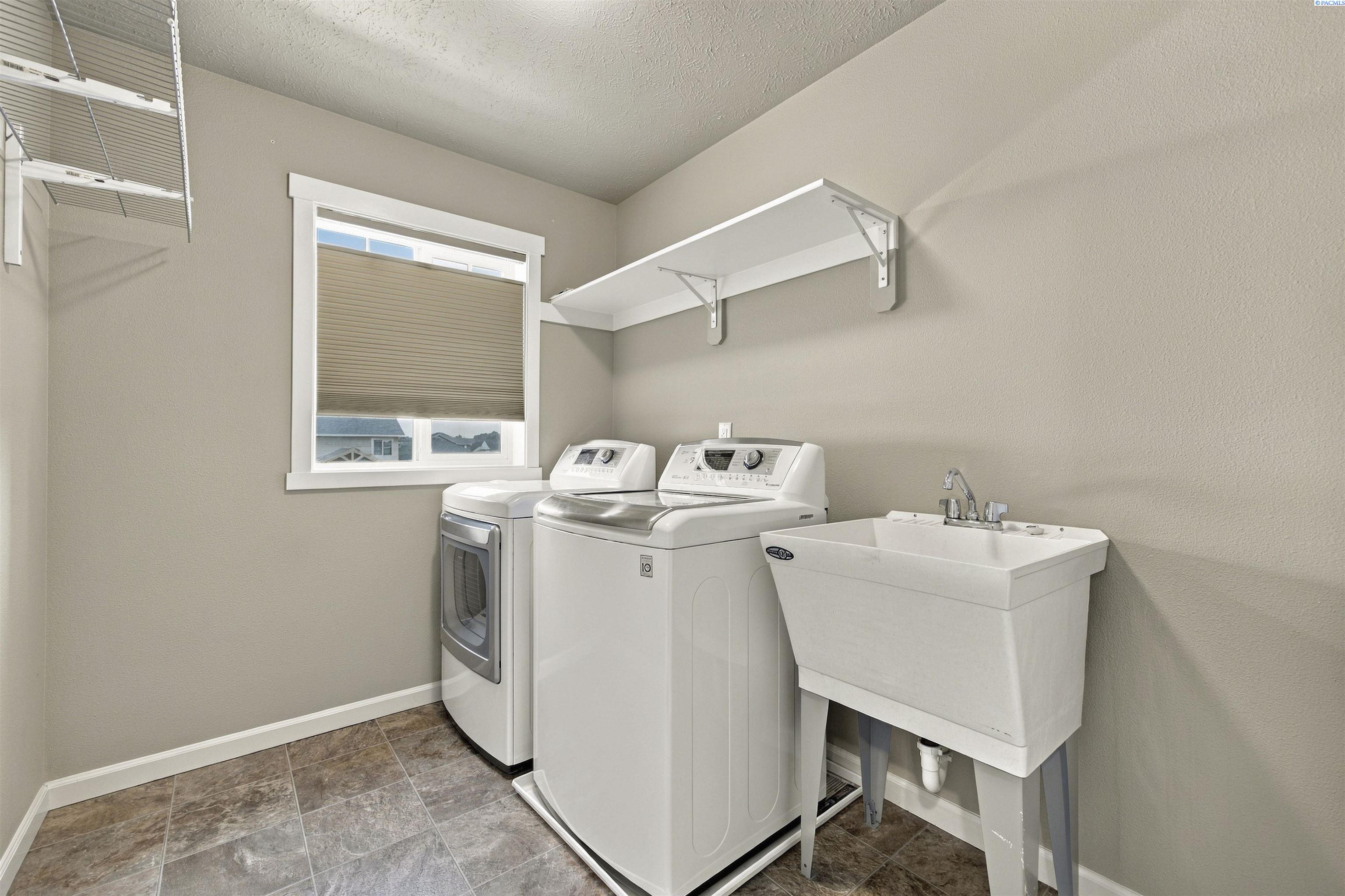 Laundry room with washer, dryer, utility sink, and wall-mounted storage shelves.
