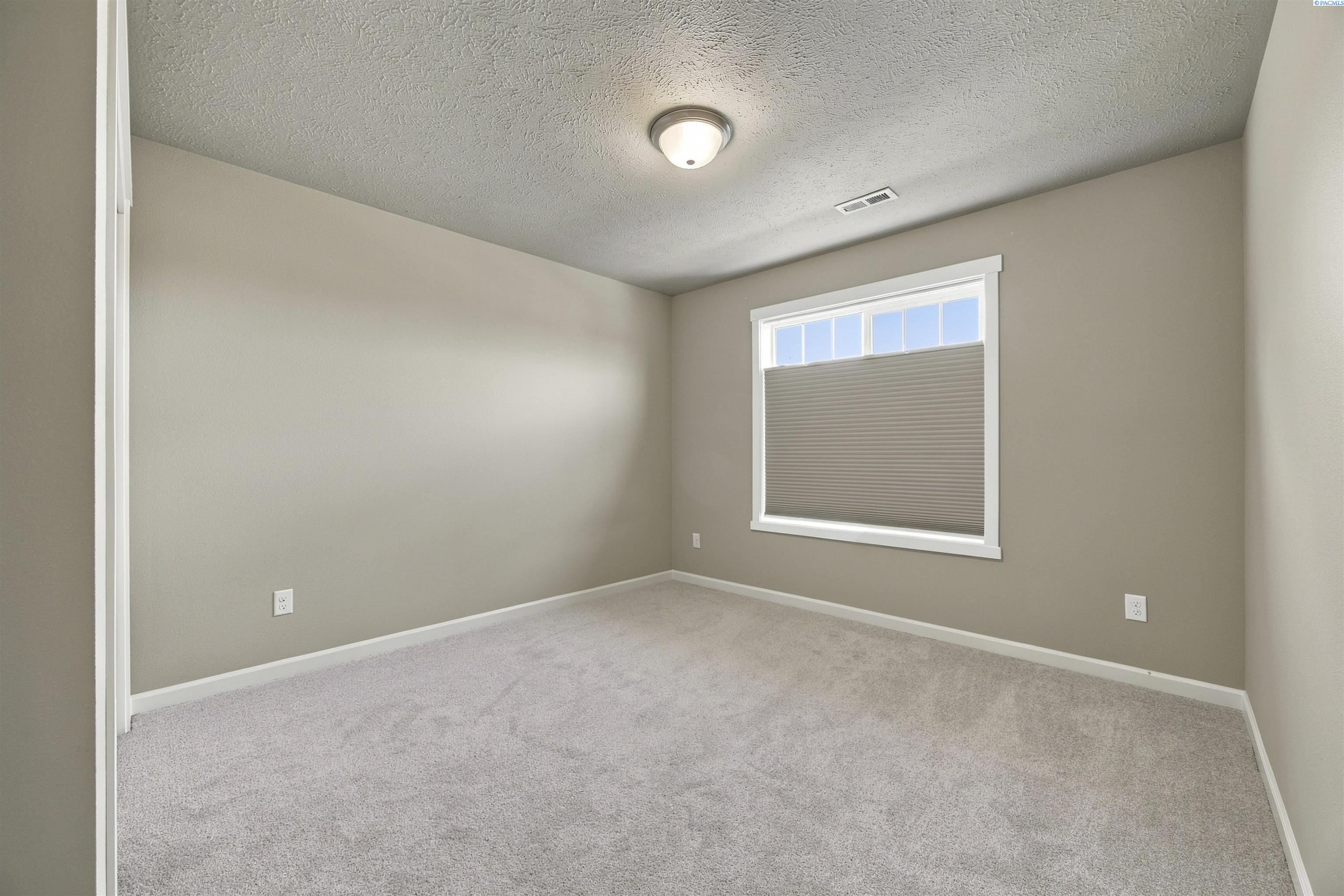 Empty carpeted room with beige walls and a window shaded by a partially lowered blind.