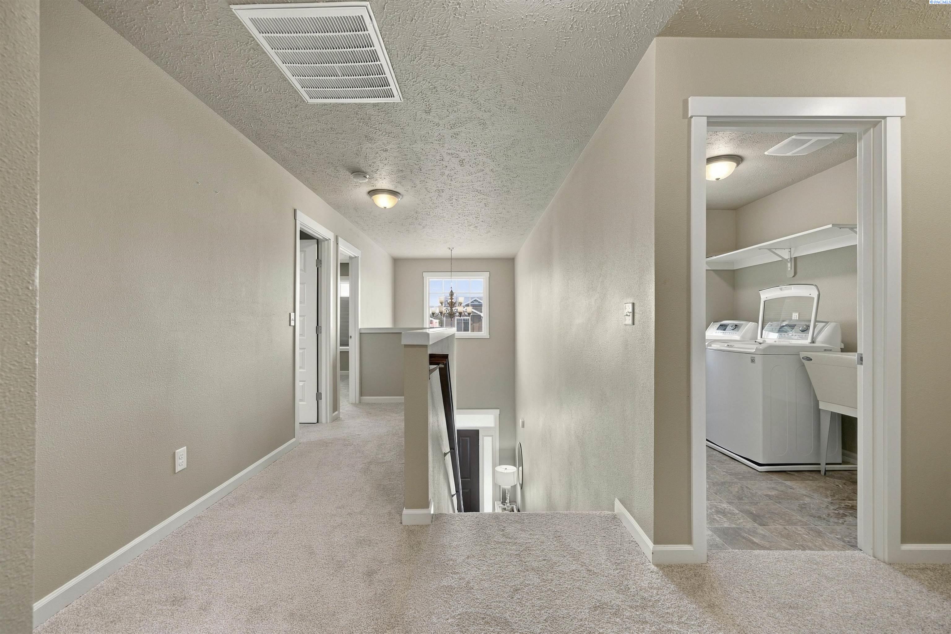 Upper-level hallway with carpeted landing, stairwell opening, and adjacent laundry room with washer and dryer.
