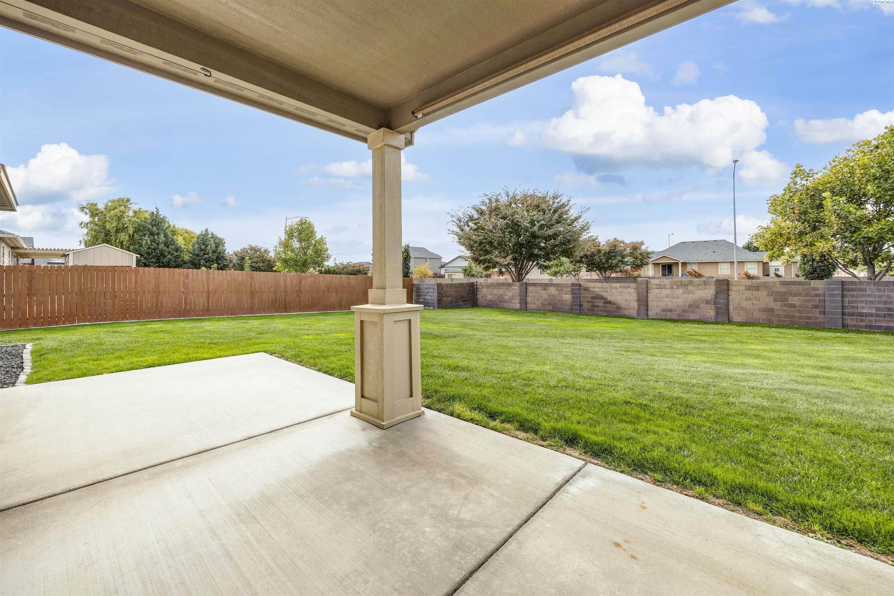 Covered concrete patio overlooking a green lawn enclosed by wood and block fences.