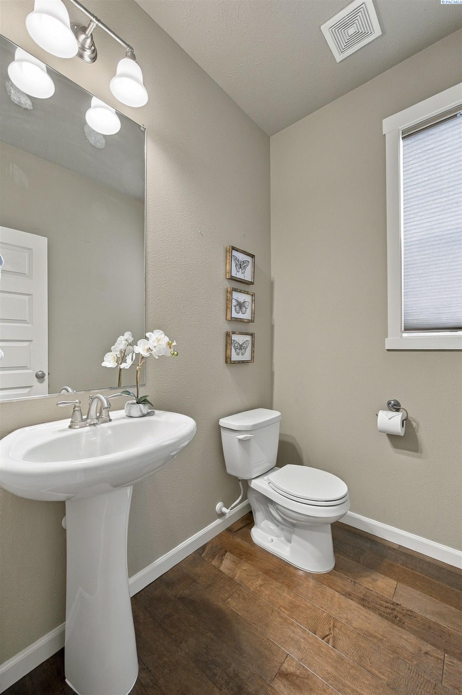 Bathroom with a pedestal sink, toilet, butterfly artwork, and wood-look flooring.