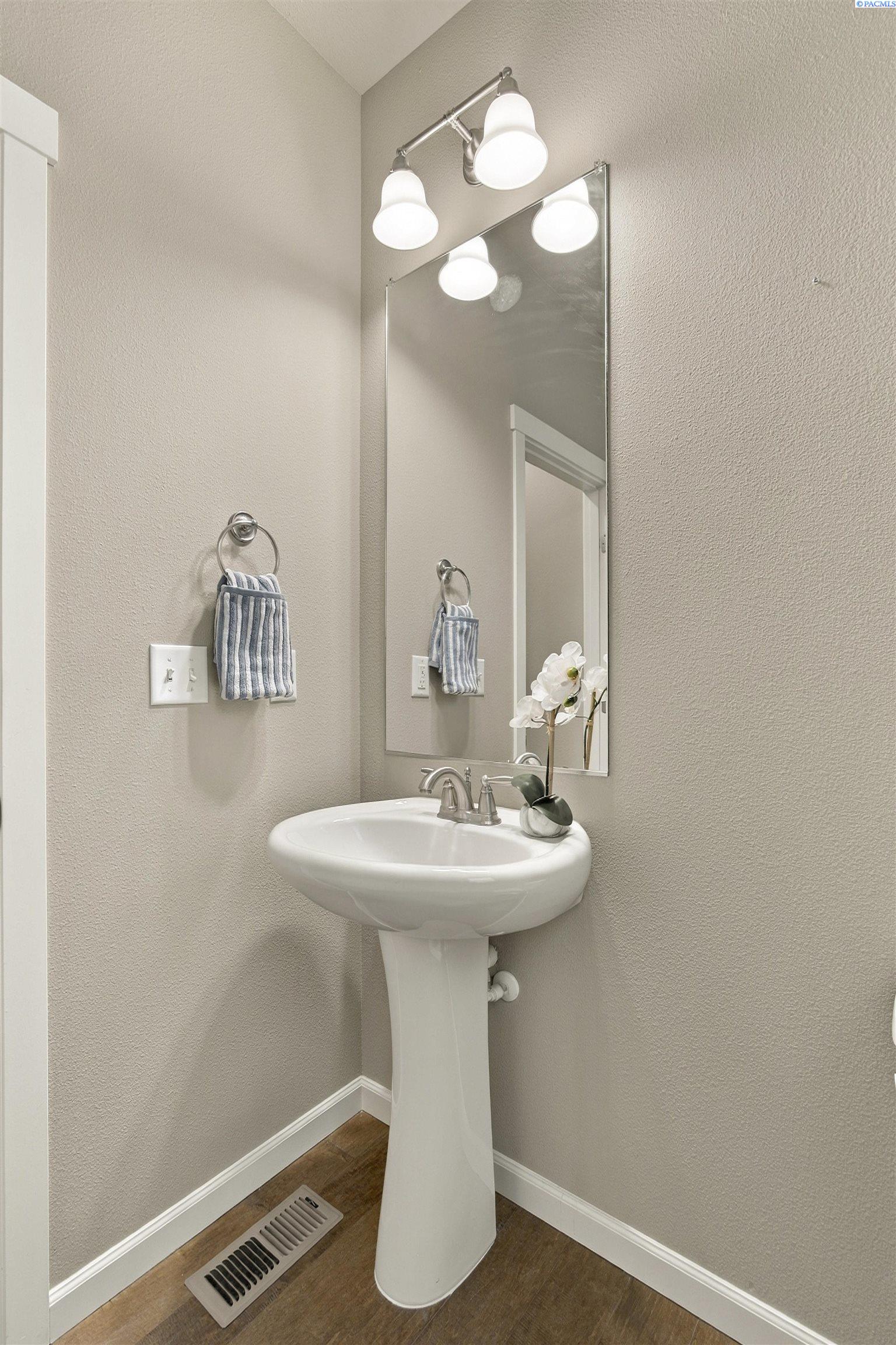 Bathroom pedestal sink with a large mirror, striped hand towel, and white orchid.