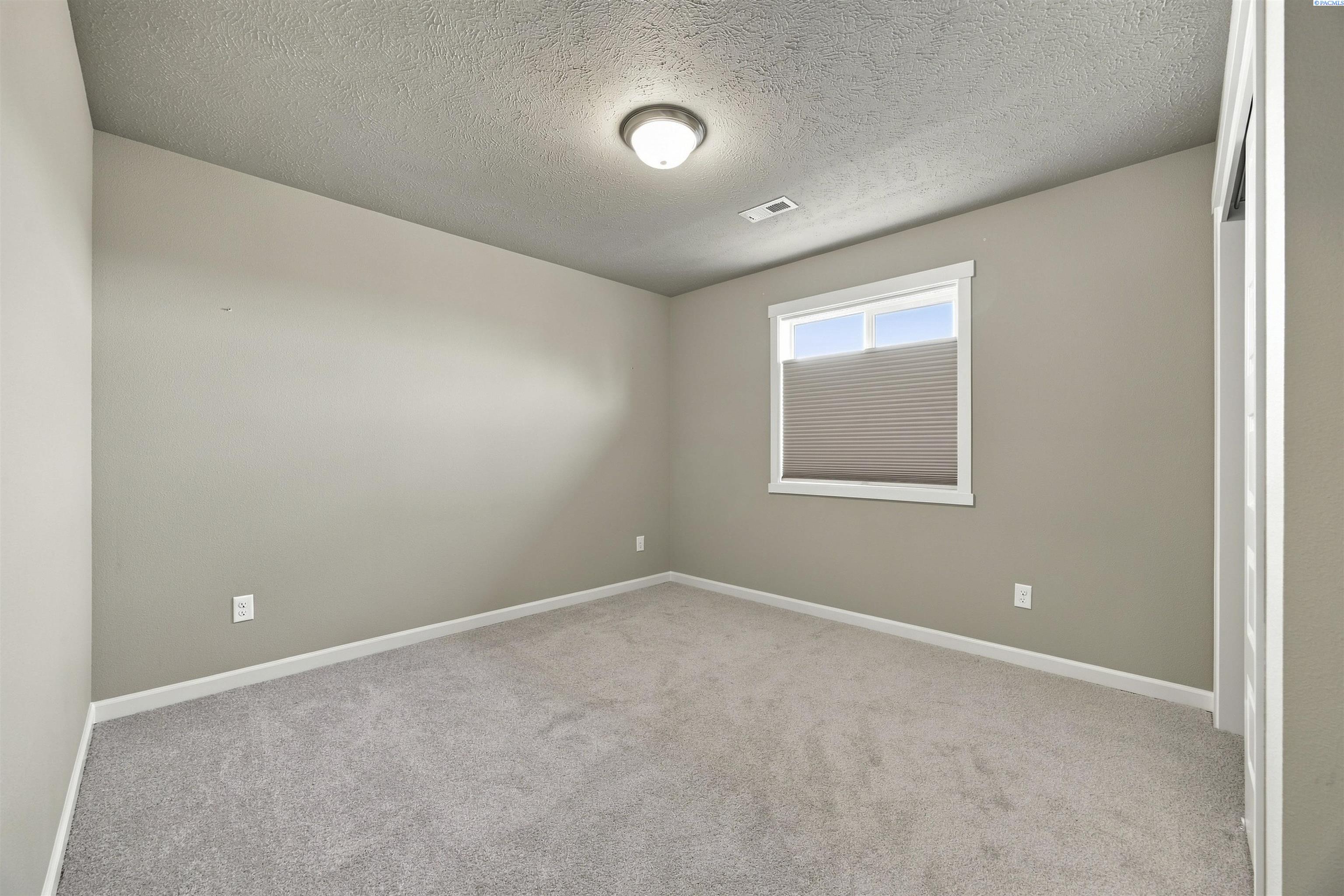 Empty carpeted room with beige walls and a window with a pleated shade.