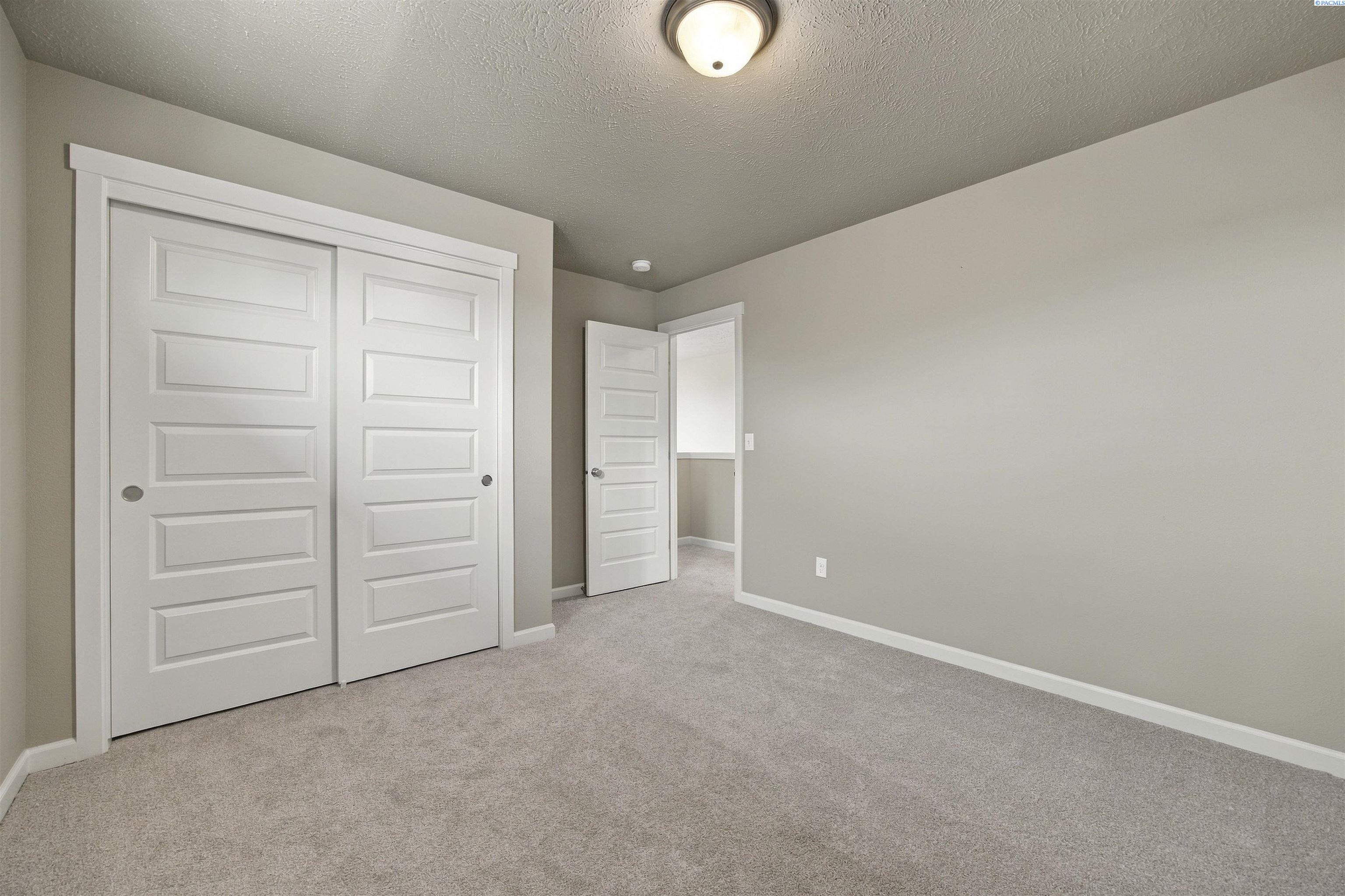 Empty carpeted room with large white closet doors and an open doorway.
