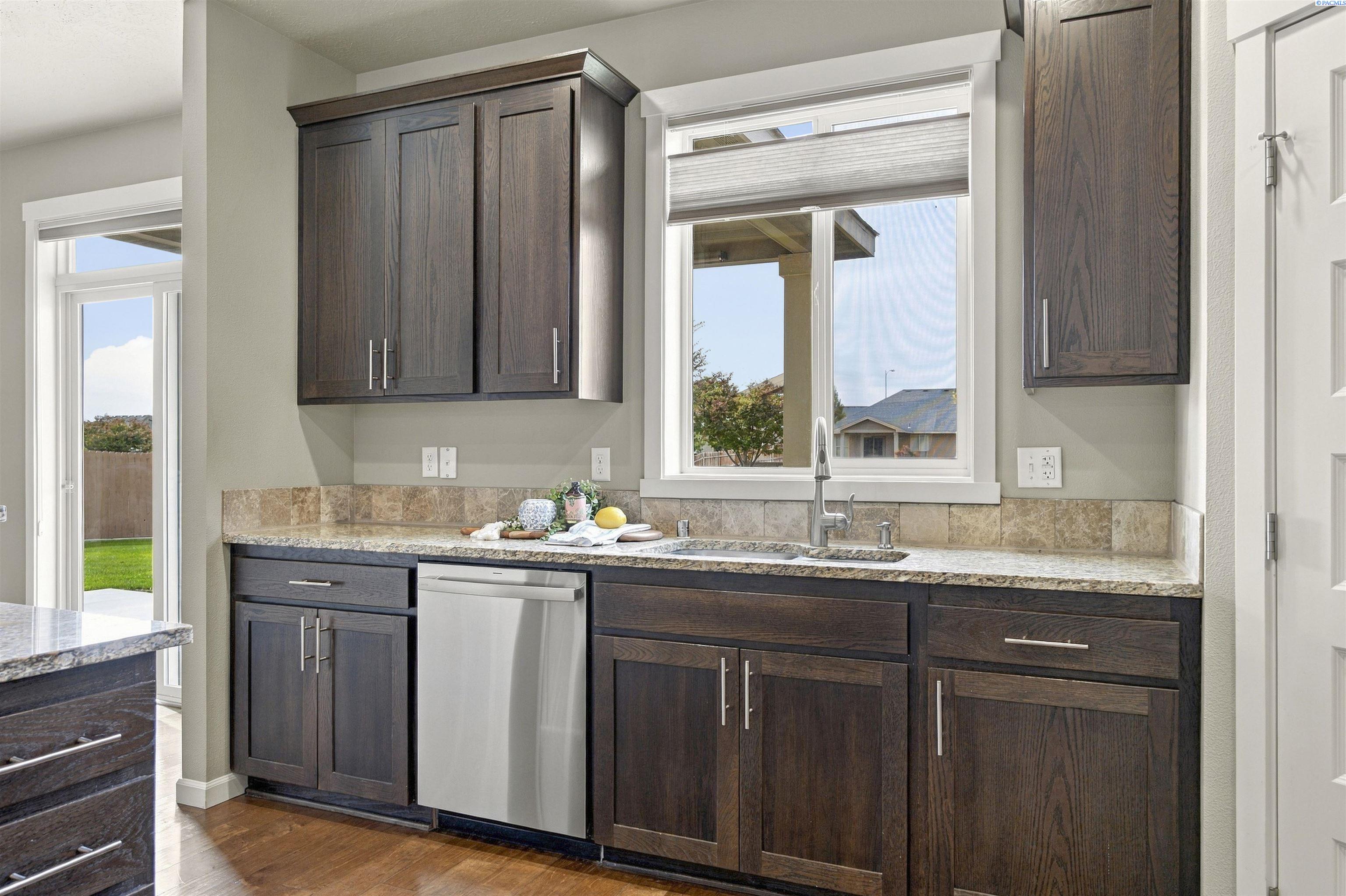 Kitchen with dark wood cabinets, granite counters, and a sink beneath a large window.
