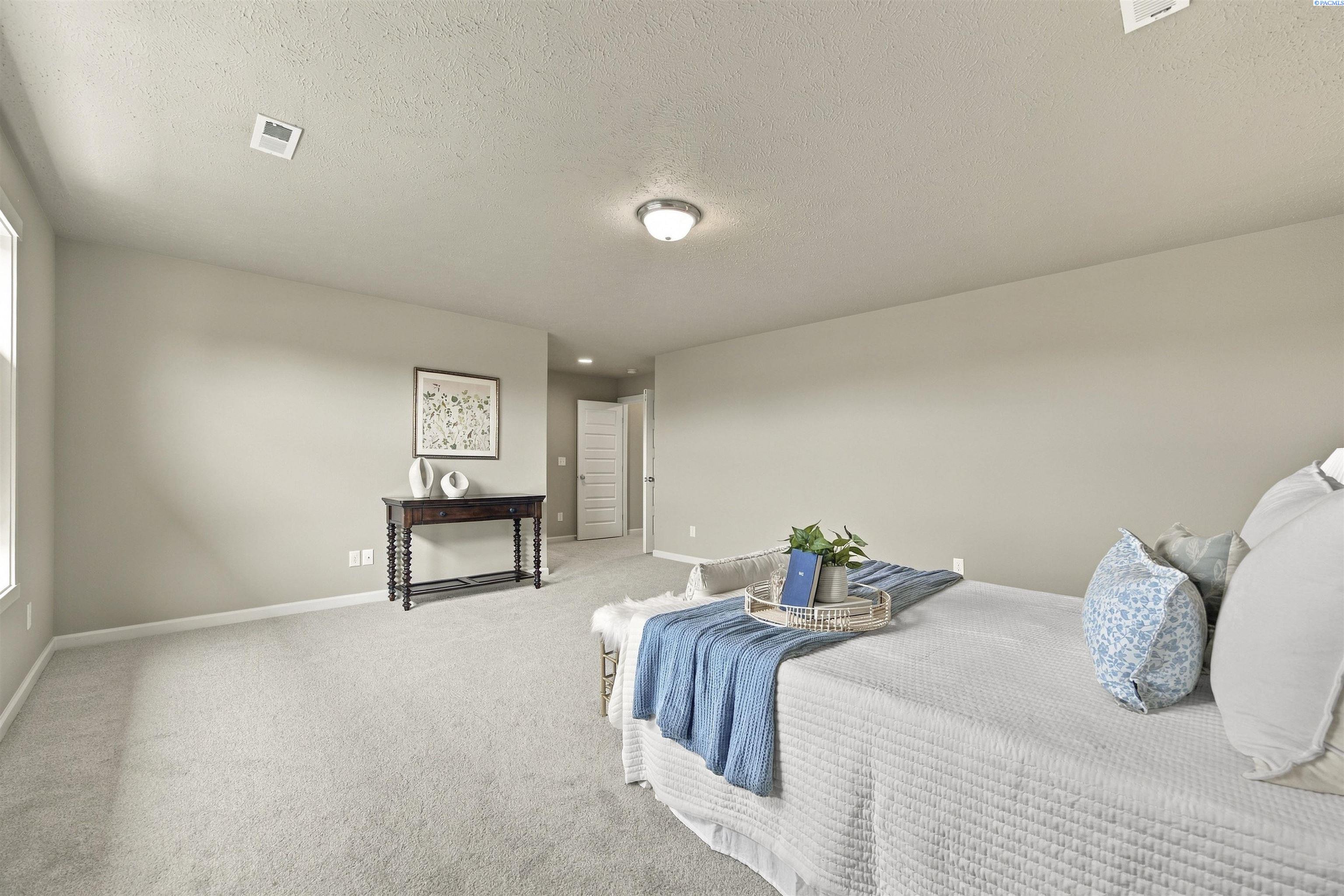 Staged bedroom with a white bed, blue throw, light carpet, and dark console table.
