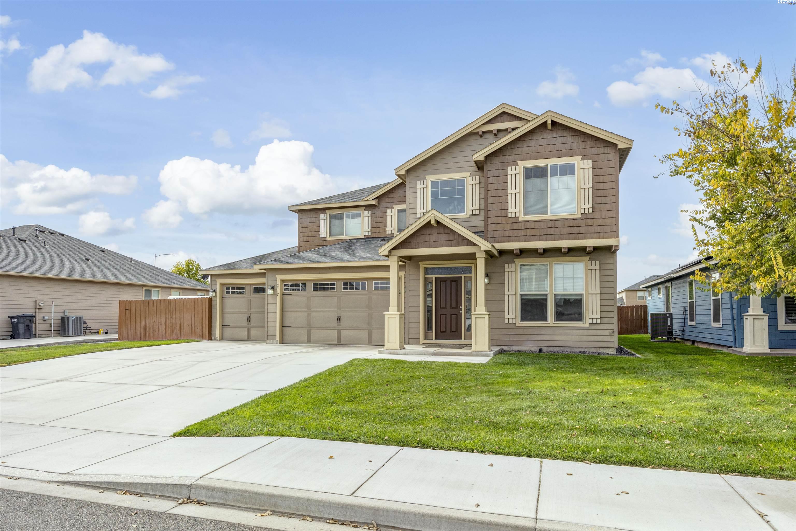 Two-story brown-and-tan house with a covered entry, three garage doors, and a wide driveway.