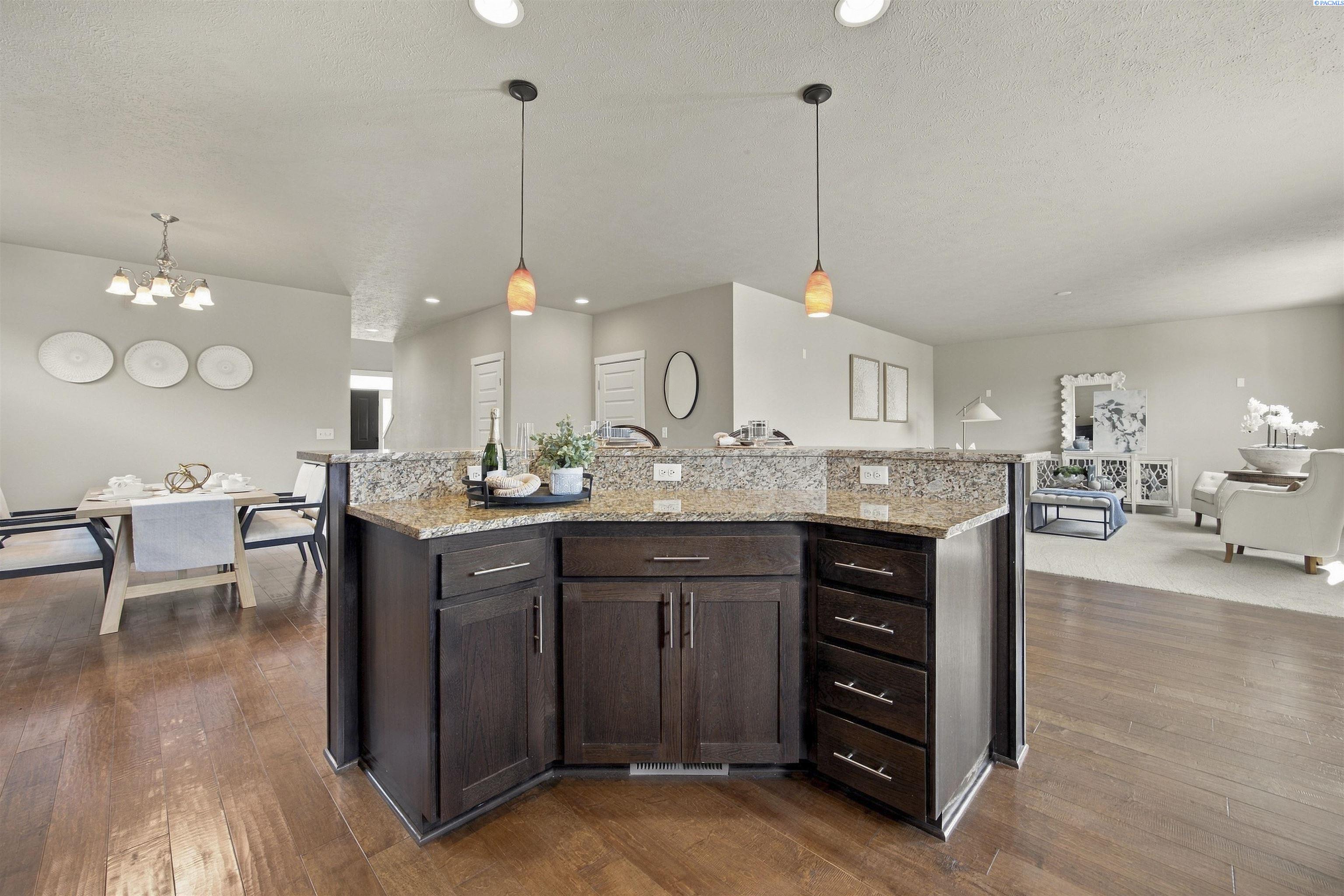 Open-plan kitchen with a large granite island, dark cabinetry, and adjoining dining and living areas.