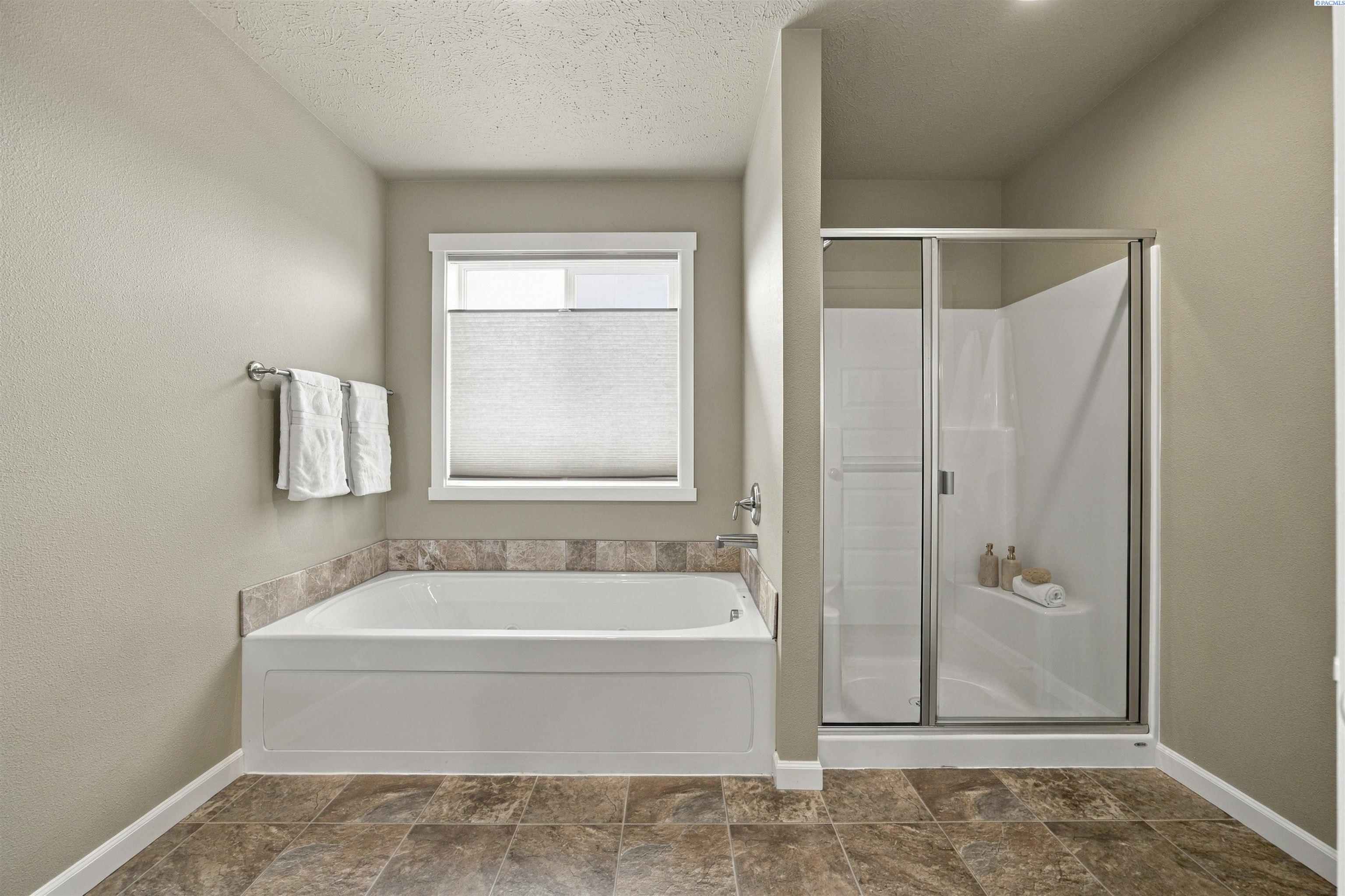 Bathroom with a white bathtub beneath a window and a separate glass-enclosed shower.