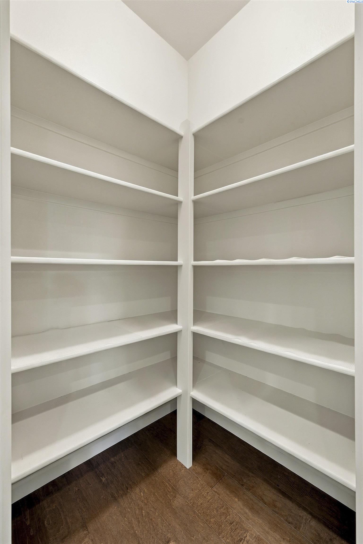 Walk-in closet with empty white corner shelves and dark wood flooring.