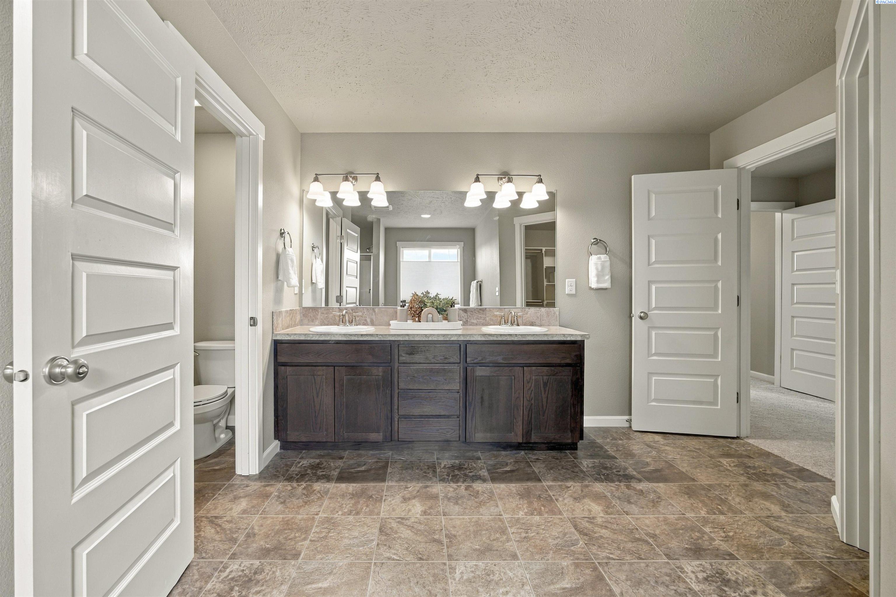 Bathroom with a dark wood double vanity, broad mirror, and brown tiled floor.