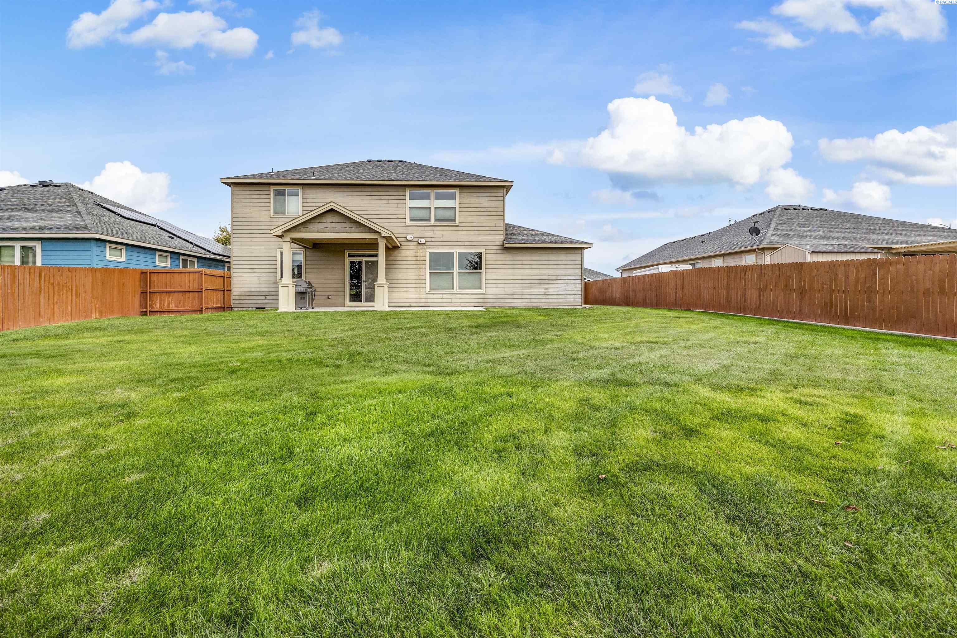 Two-story beige home behind a broad, fenced backyard lawn.