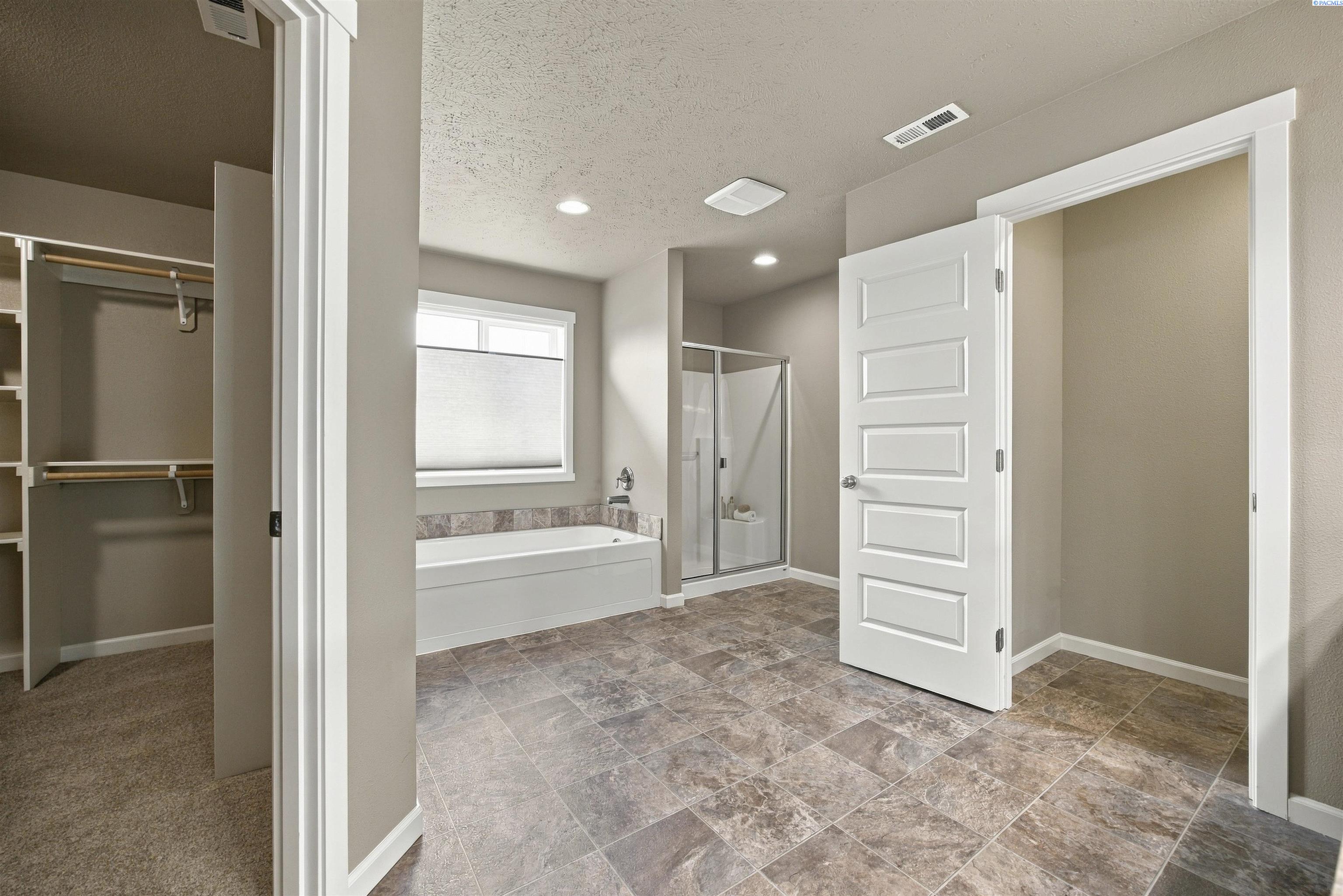Bathroom with a built-in tub, glass shower, and adjoining walk-in closet.