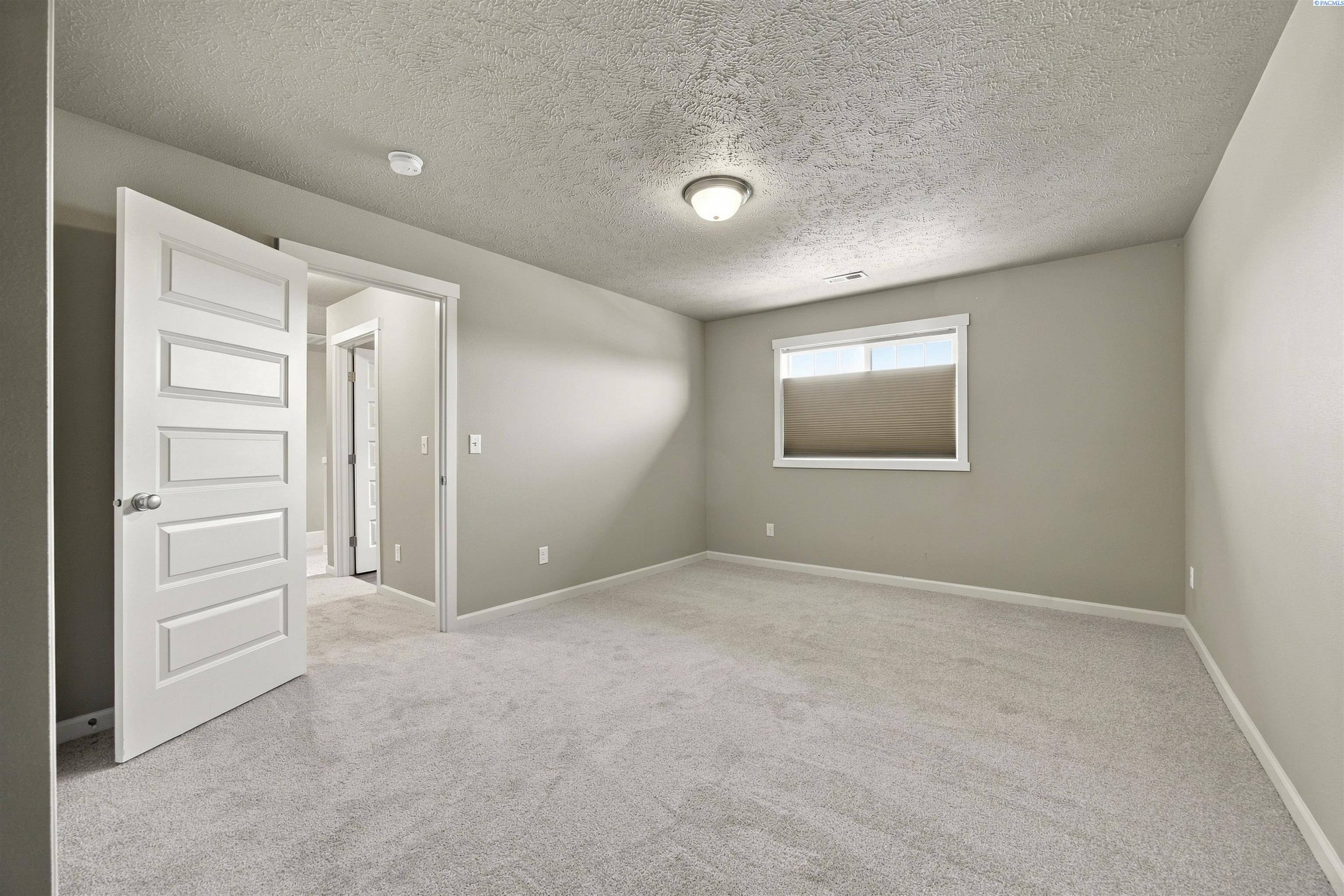 Empty carpeted bedroom with neutral walls, a shaded window, and an open paneled door.