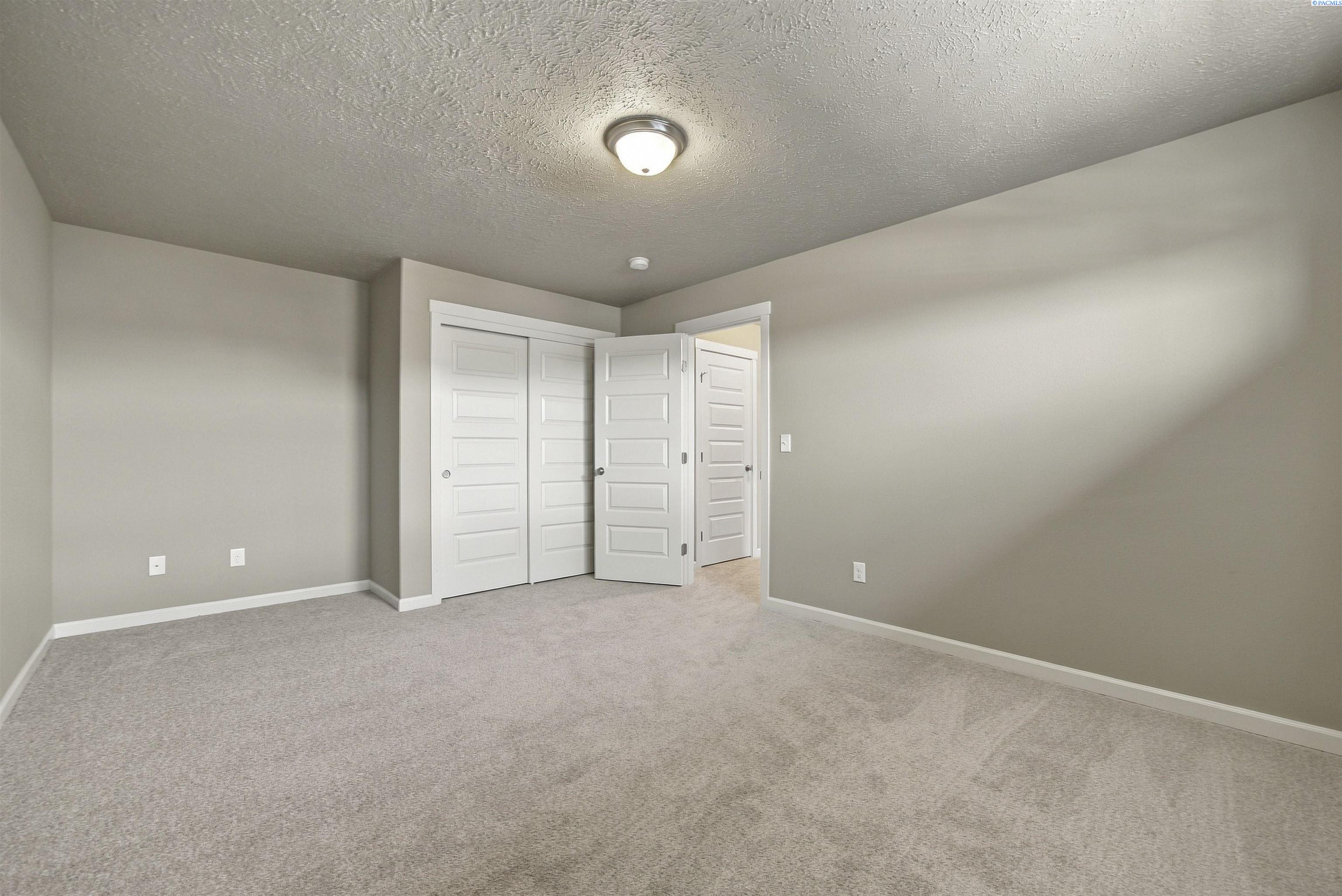 Empty bedroom with beige carpet, paneled white closet doors, and an open door to the hall.