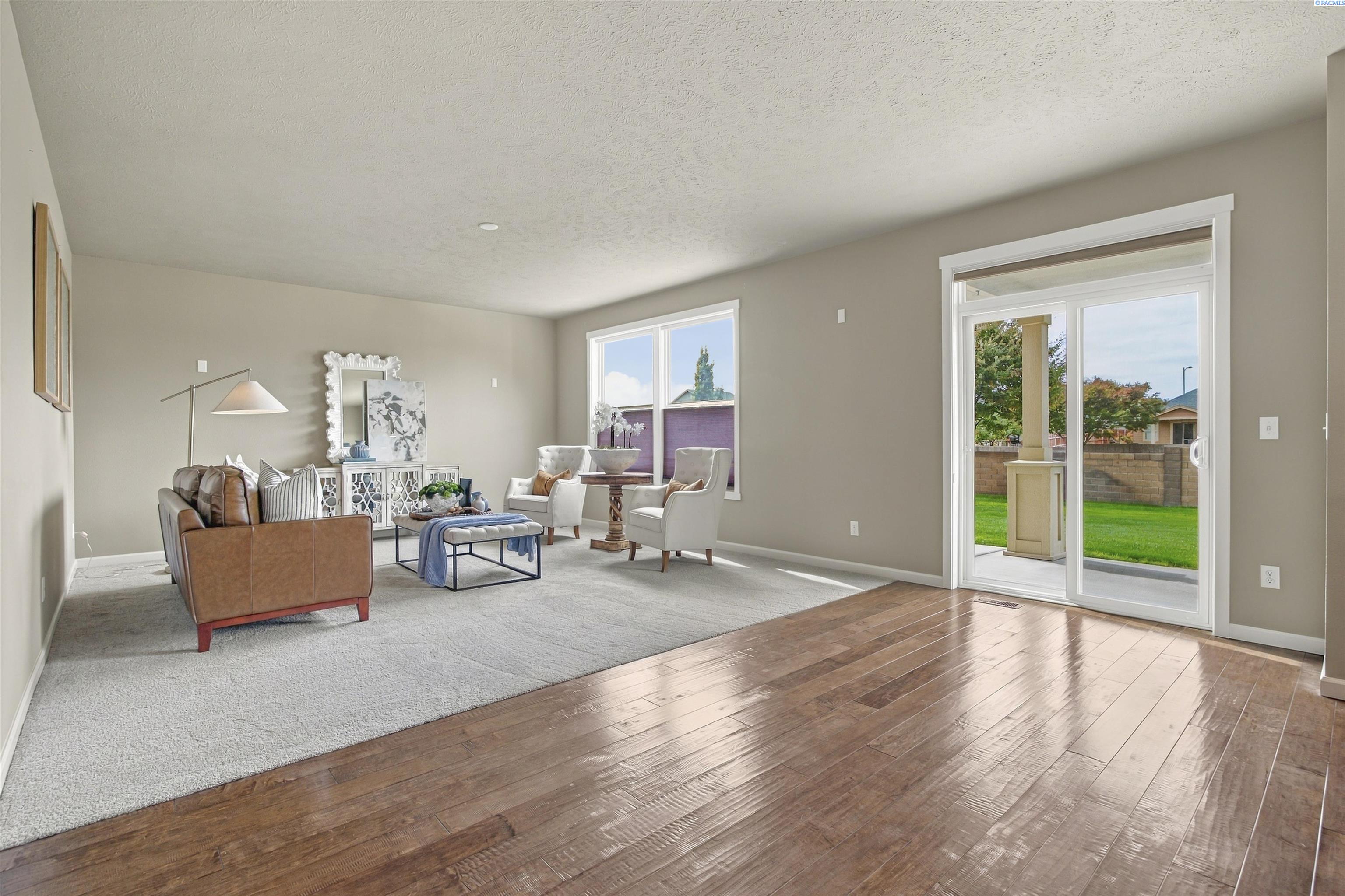 Staged living room with a leather sofa, white armchairs, and sliding glass doors to the backyard.