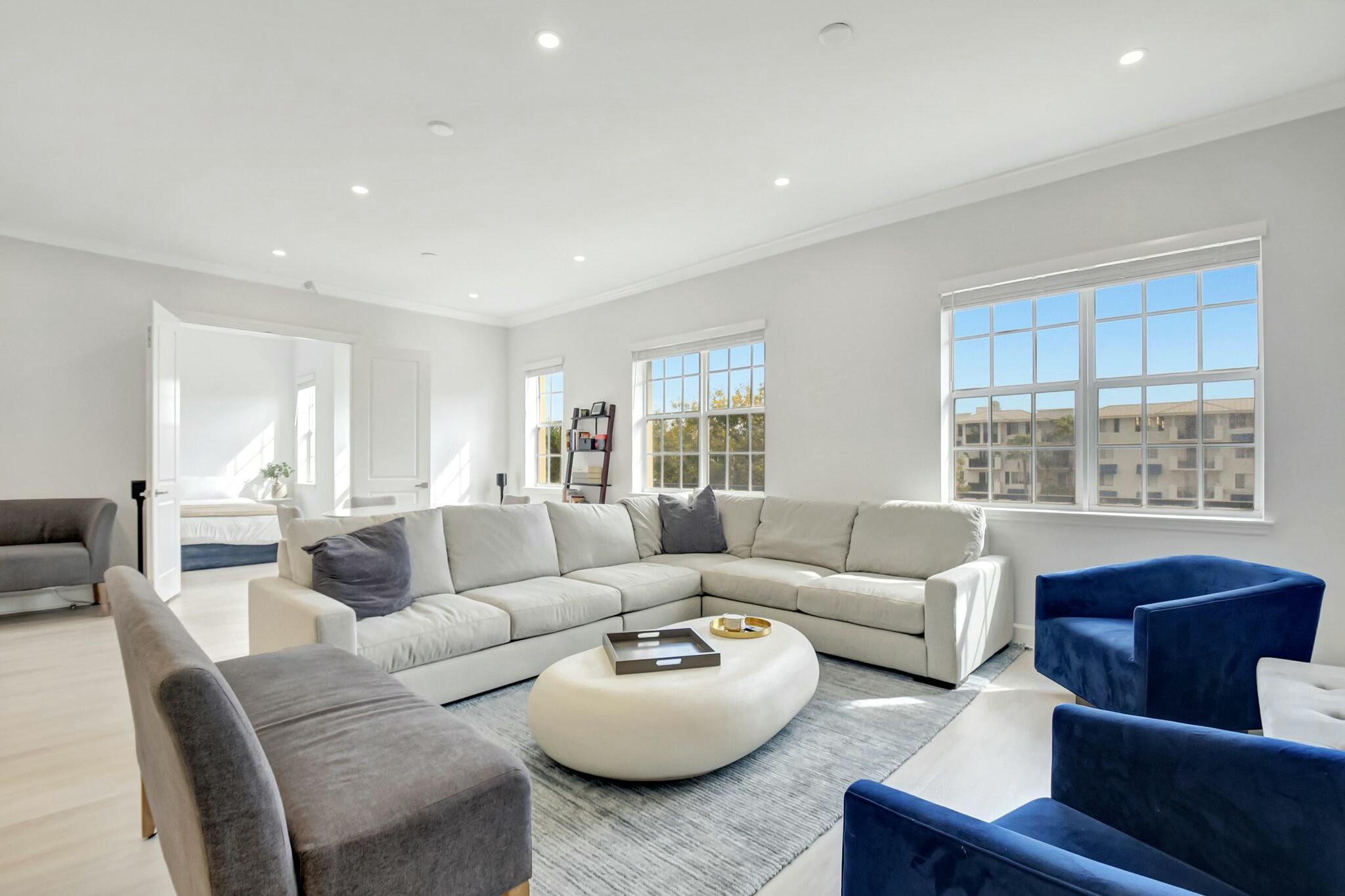 Bright living room with a white sectional, blue accent chairs, and large windows.