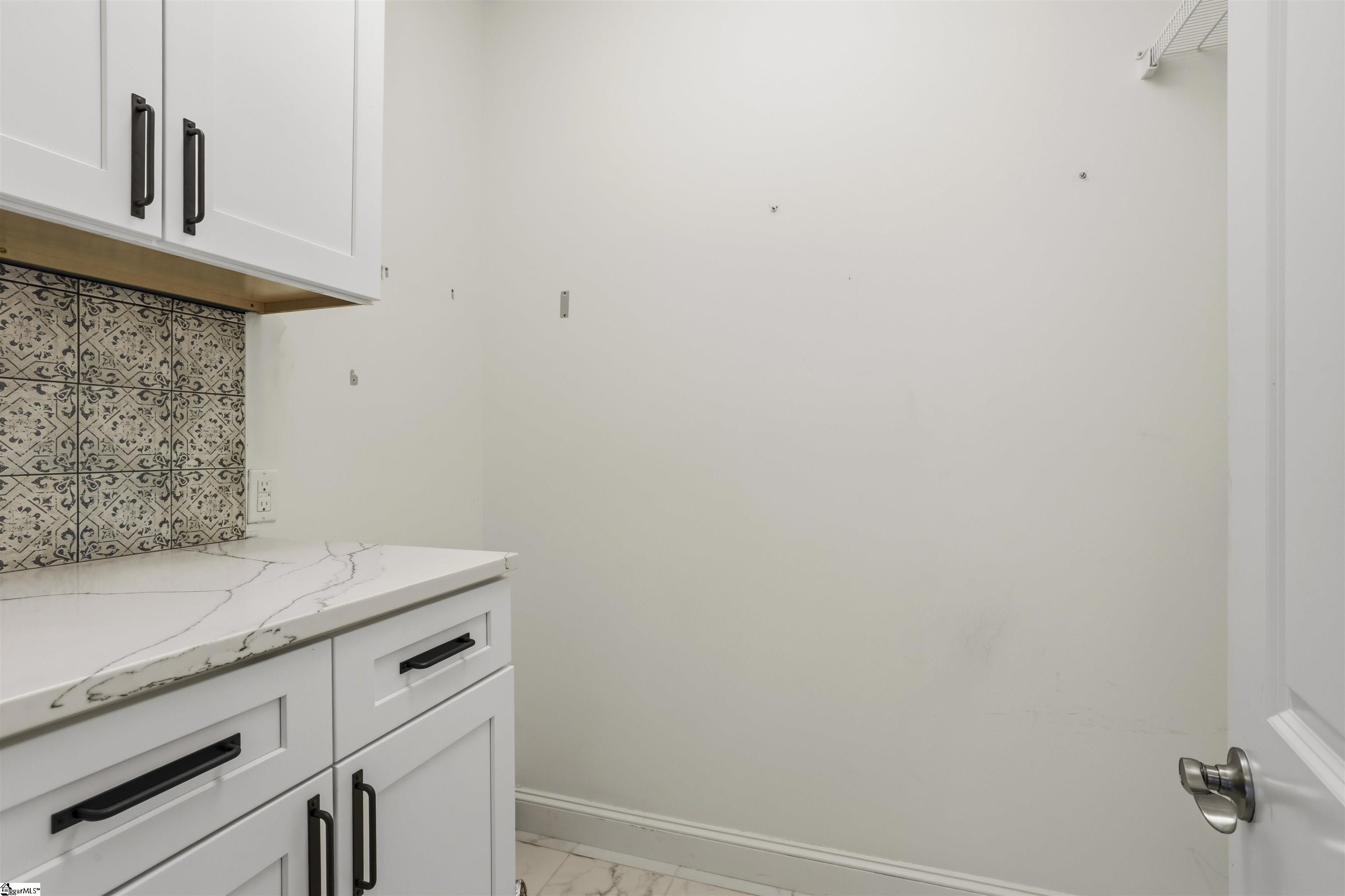 White cabinets and veined countertop beside patterned tile backsplash and an open appliance space.