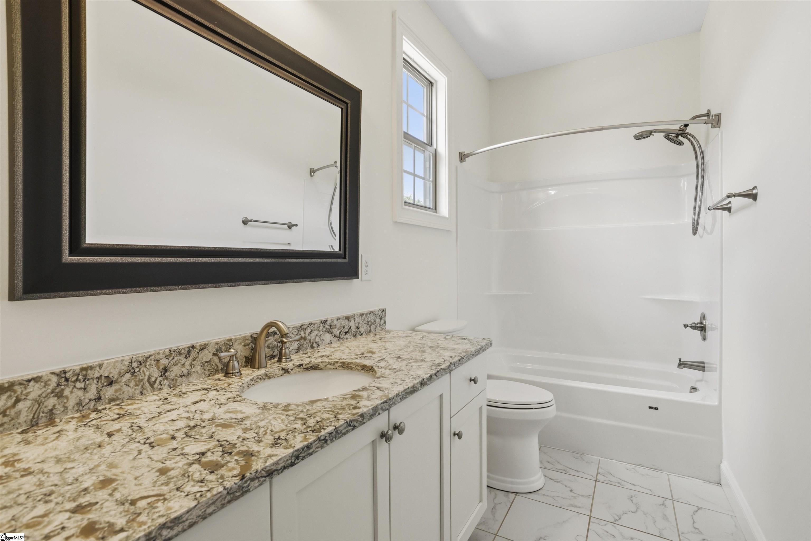 Bathroom with a granite vanity, dark-framed mirror, and white tub-shower beneath a tall window.