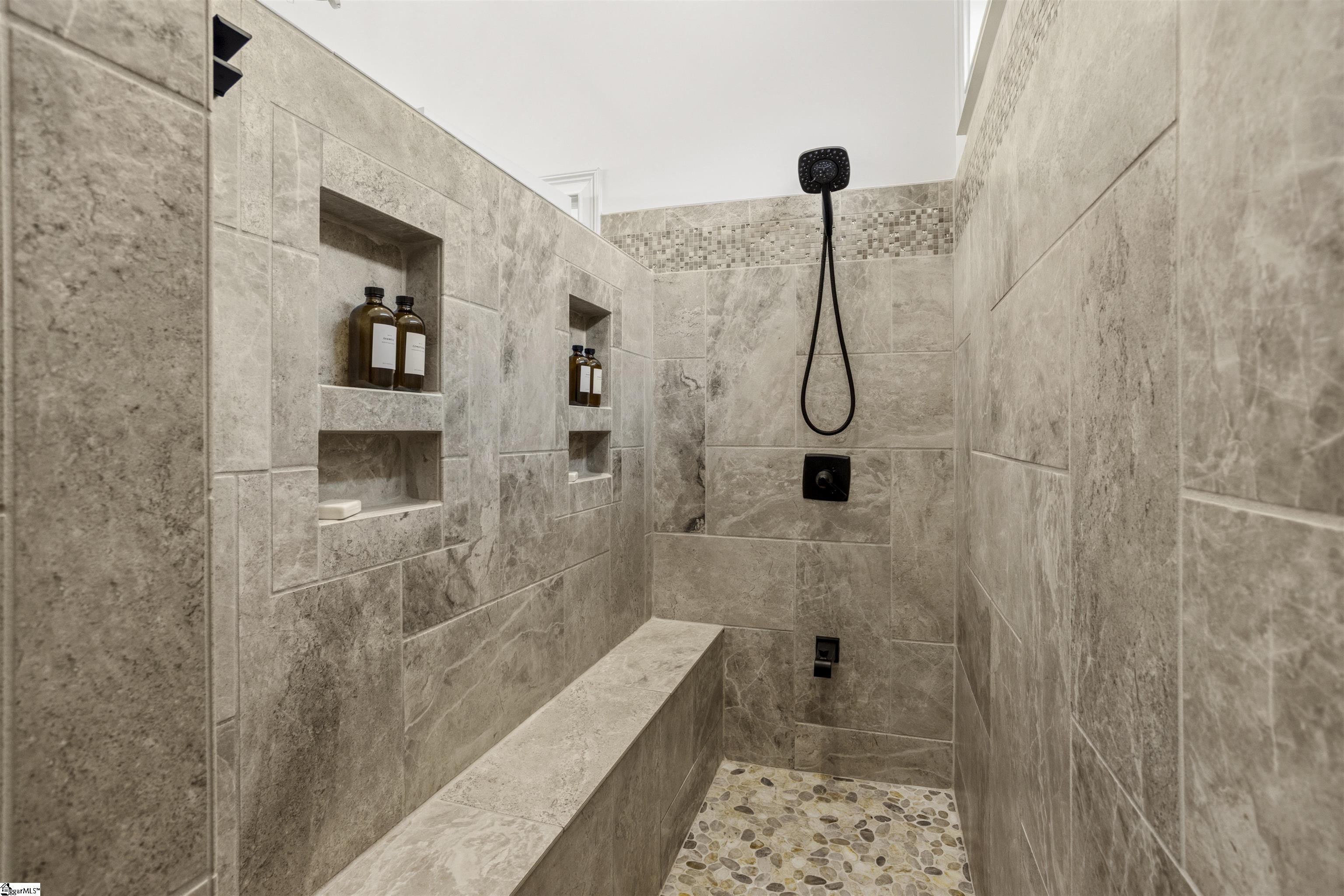 Walk-in shower with built-in niches, a tiled bench, pebble floor, and black fixtures.
