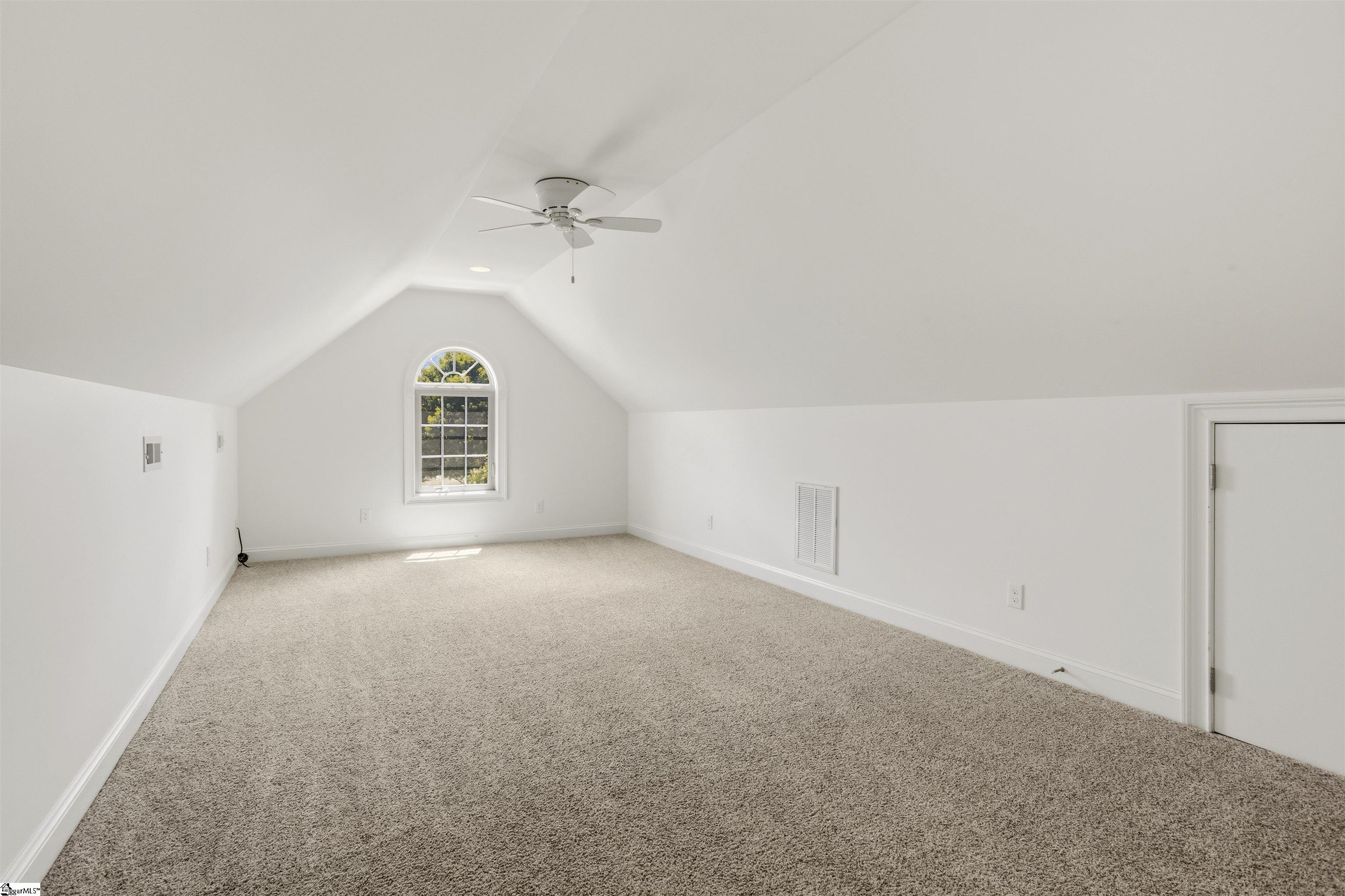 Empty carpeted room with a vaulted ceiling, ceiling fan, and arched window.