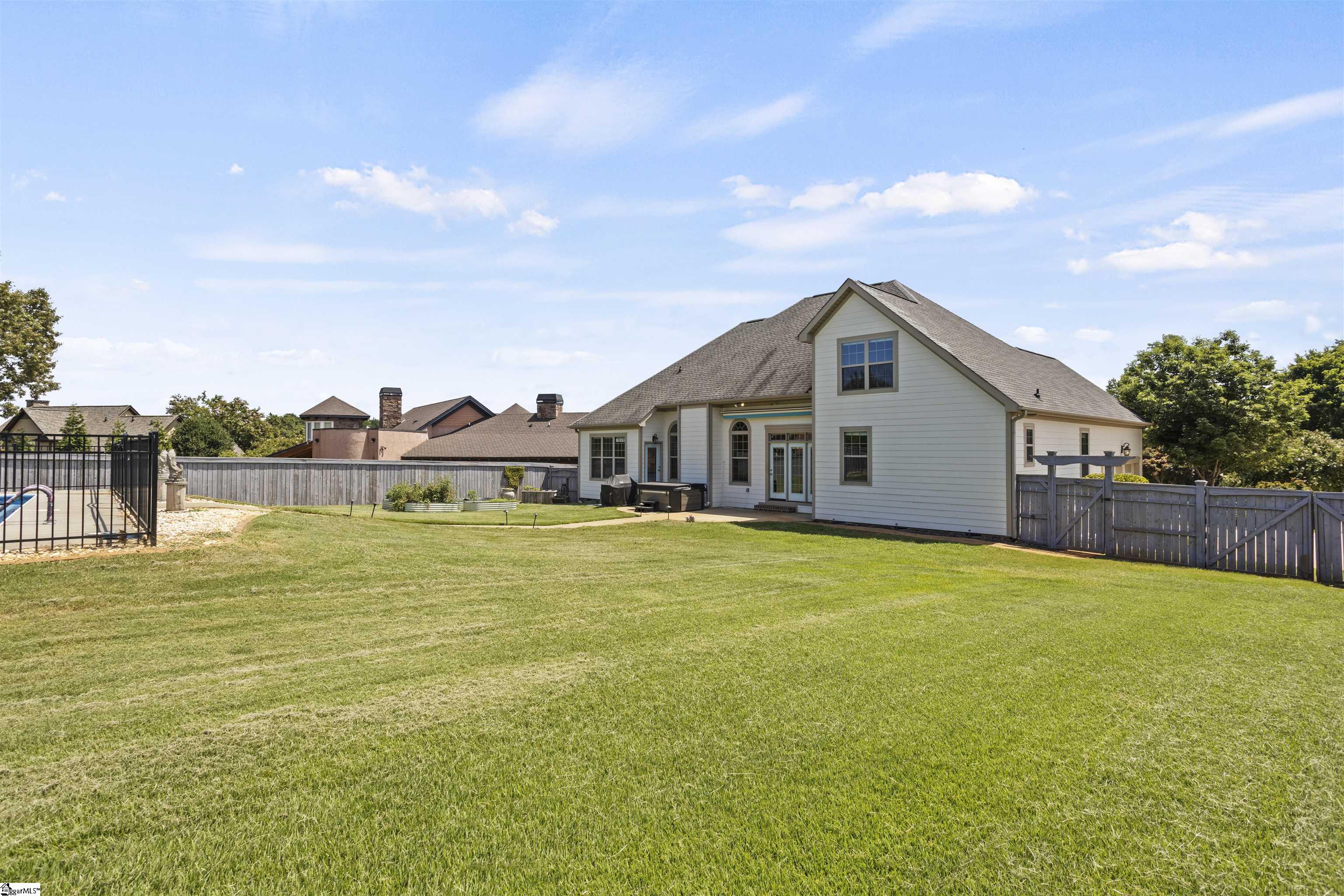 Rear of a two-story home overlooking a broad lawn, with a fenced pool at the side.
