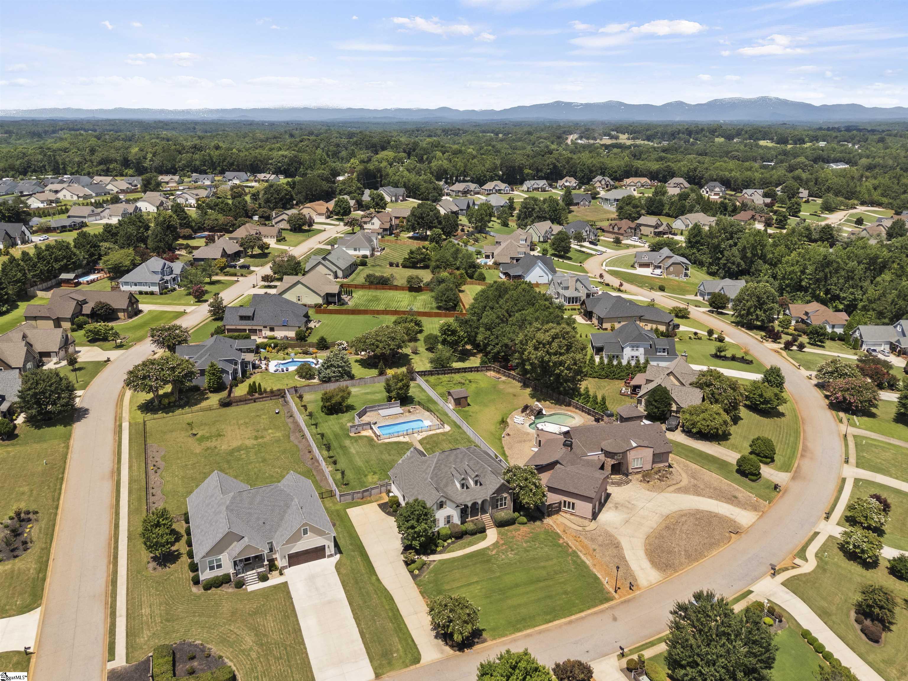 Aerial view of a suburban neighborhood with swimming pools and distant mountain views.
