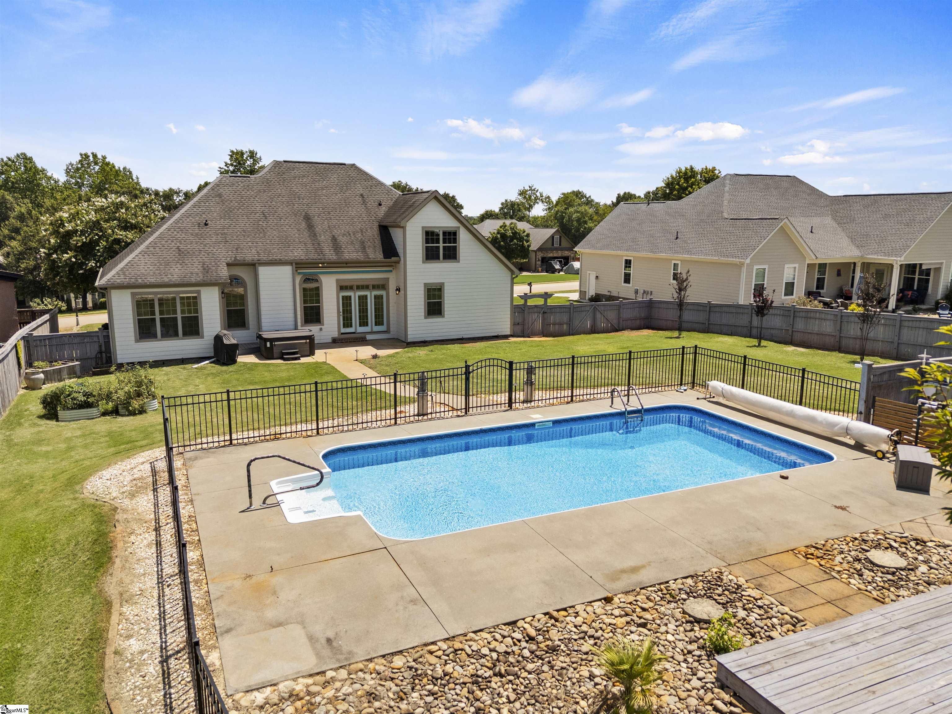 House and fenced backyard with an in-ground pool and broad concrete patio.