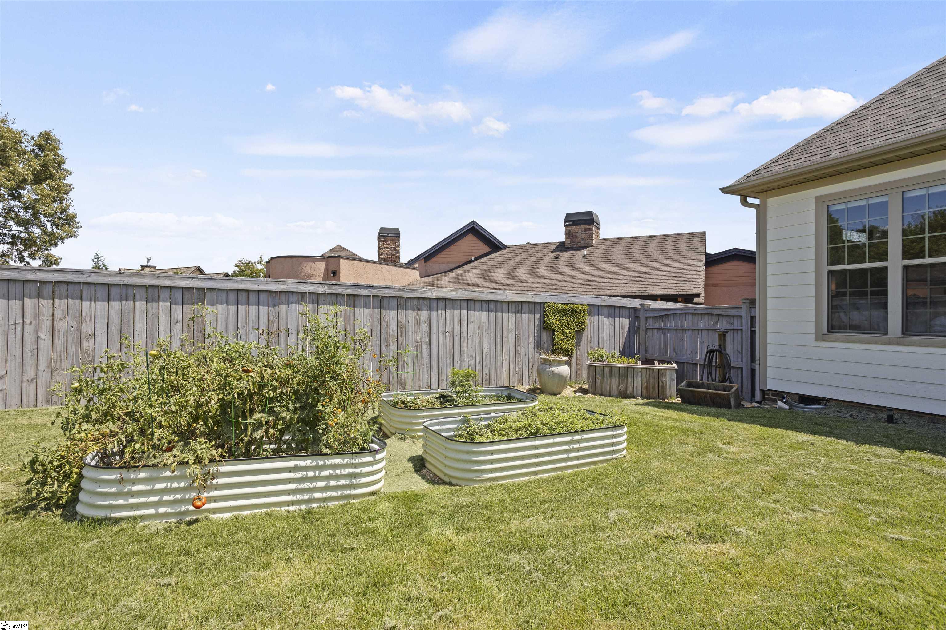 Fenced backyard with raised vegetable garden beds, lawn, and the side of a light-colored house.