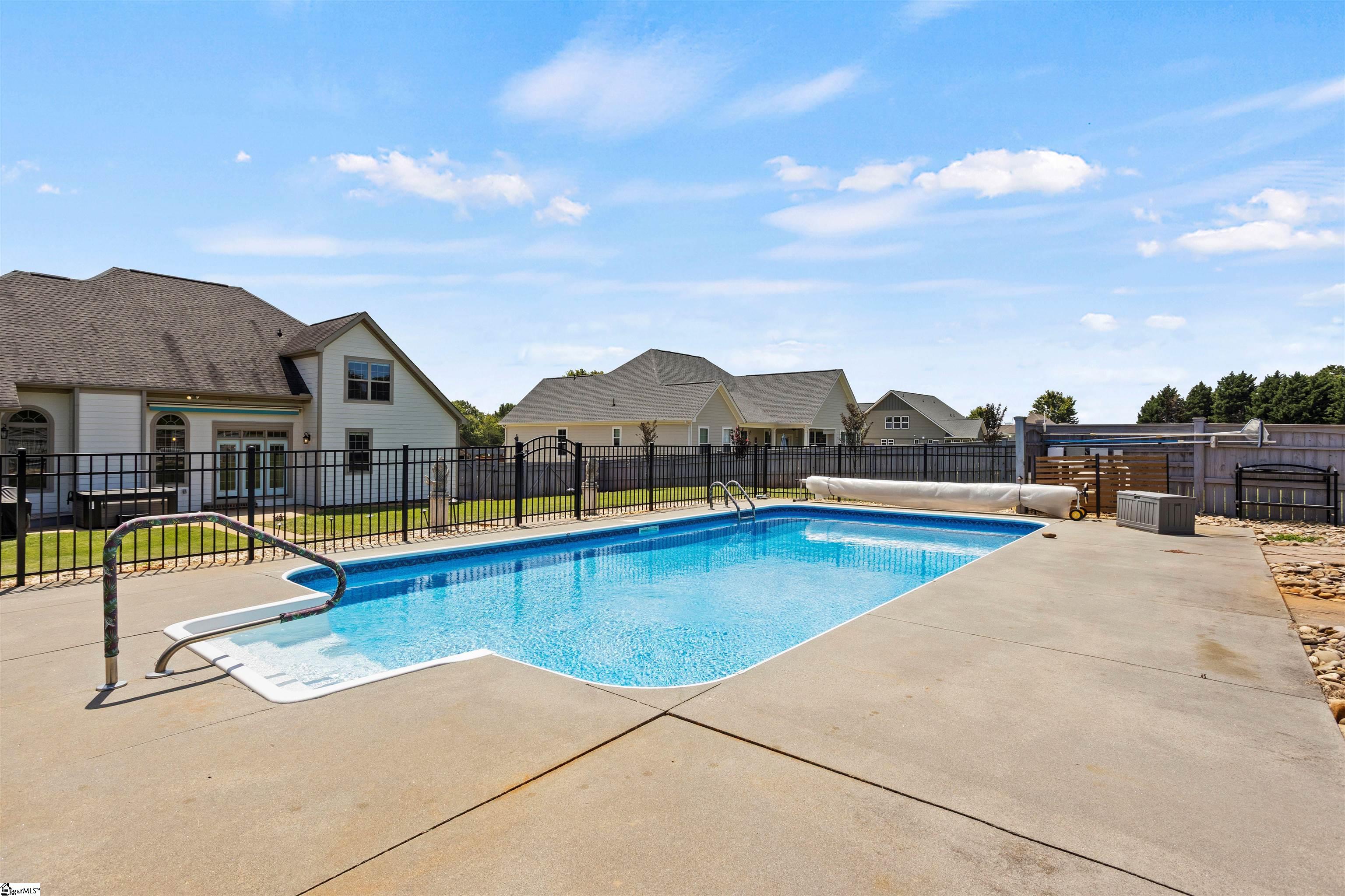 Backyard swimming pool with a wide concrete deck and metal fencing.
