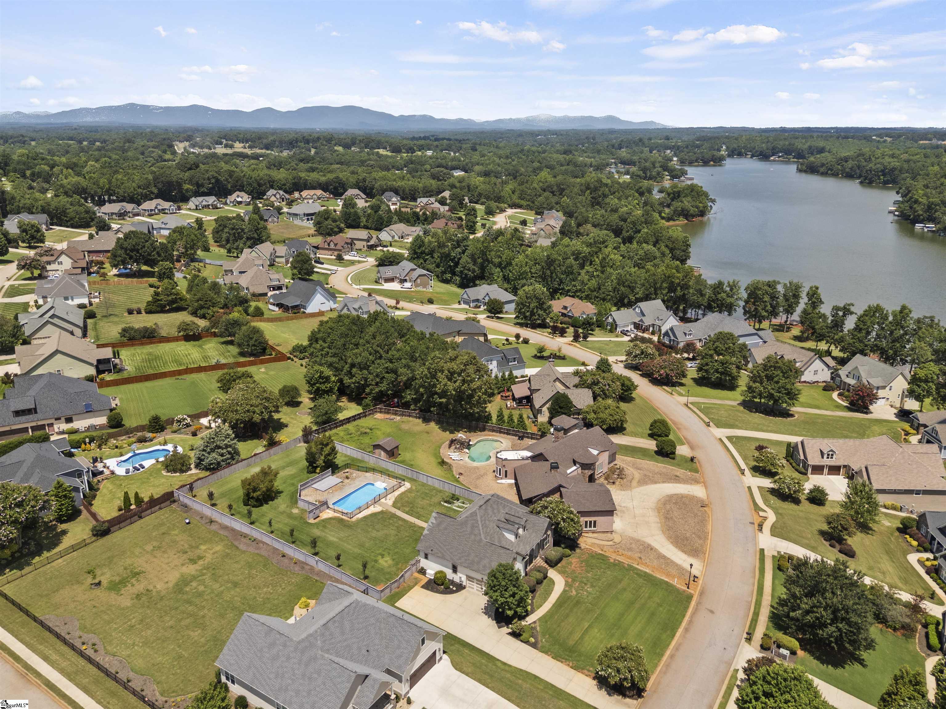 Aerial neighborhood beside a lake, with private pools and a distant mountain ridge.
