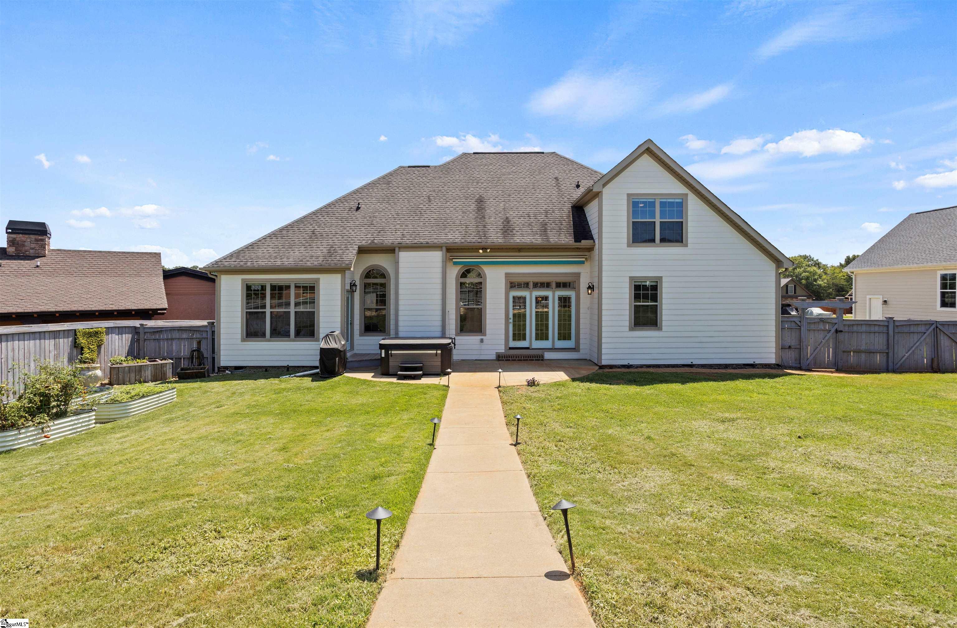Rear exterior of a two-story home with a fenced lawn, patio, hot tub, and raised garden beds.